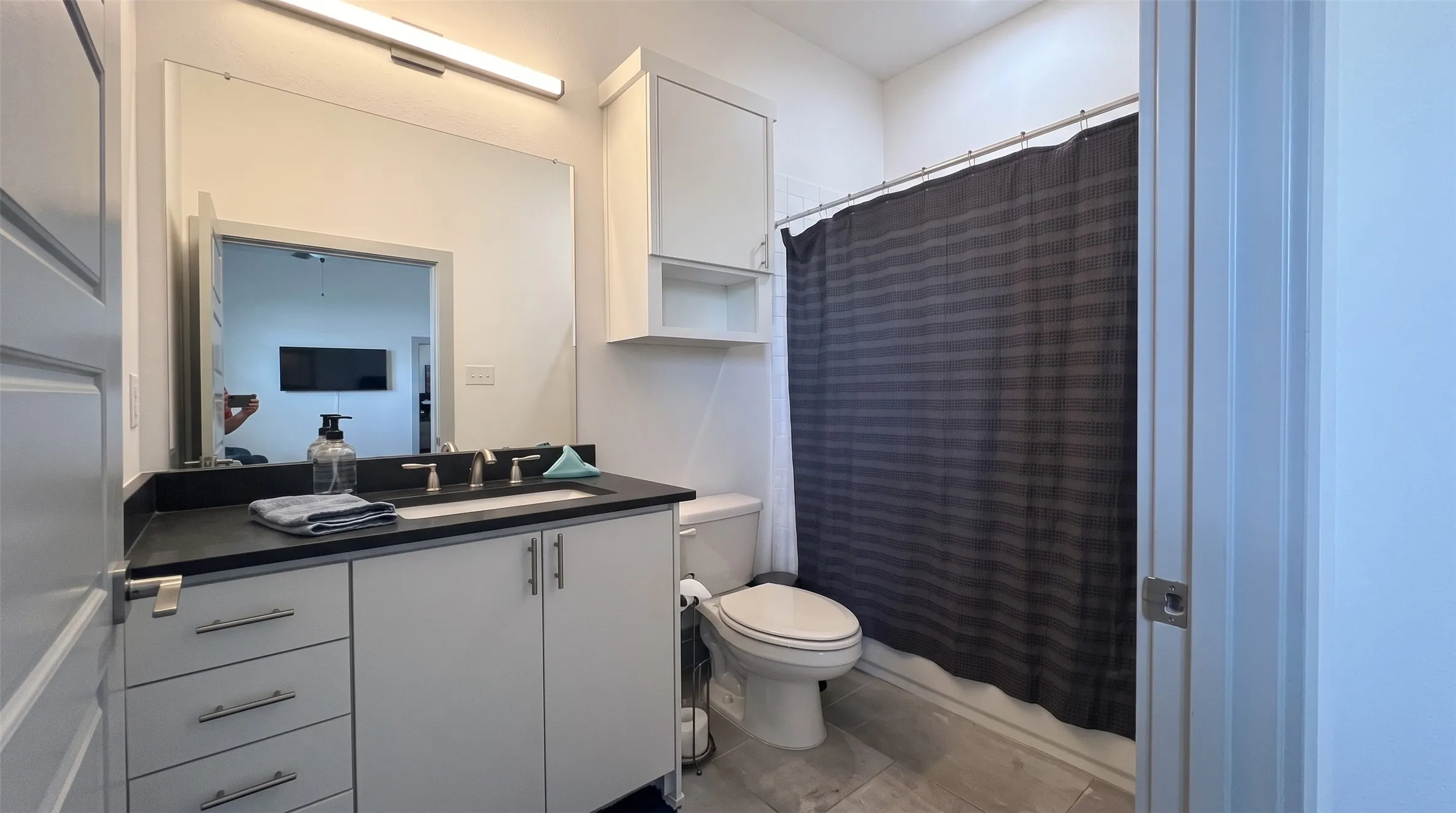 Vanity with a dark countertop and undermount sink, built-in cabinetry, and a full-width mirror