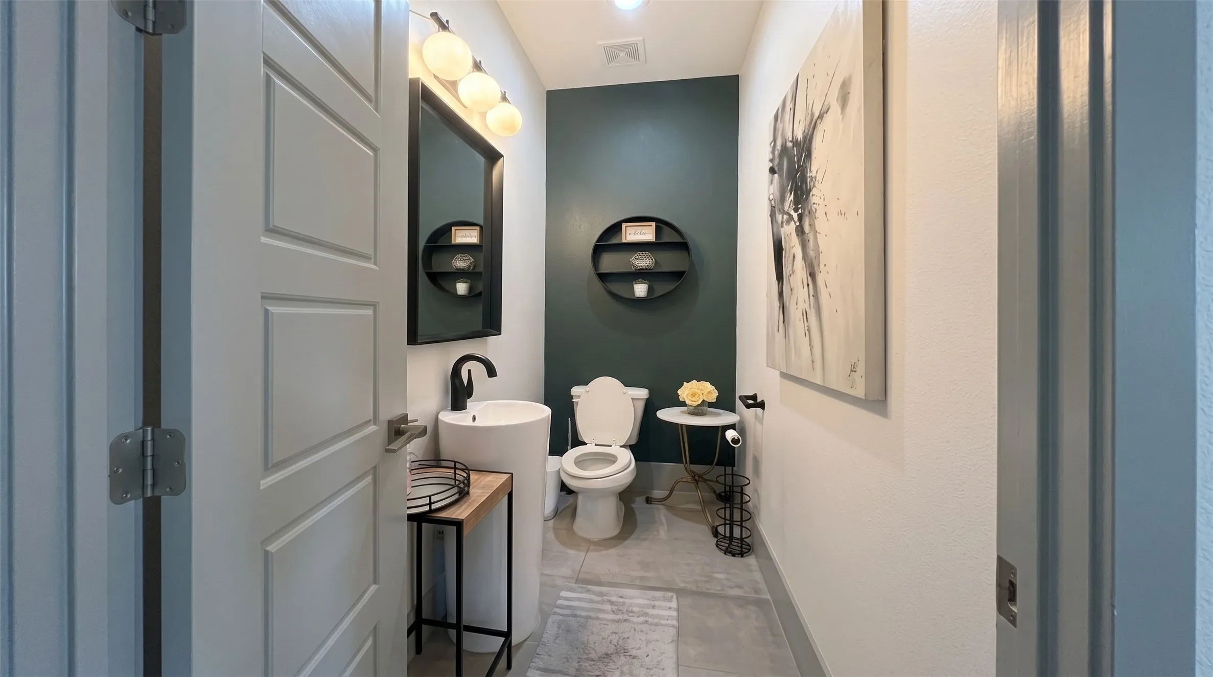 Pedestal sink with a matte black faucet, wall-mounted rectangular mirror, and three-bulb vanity lighting
