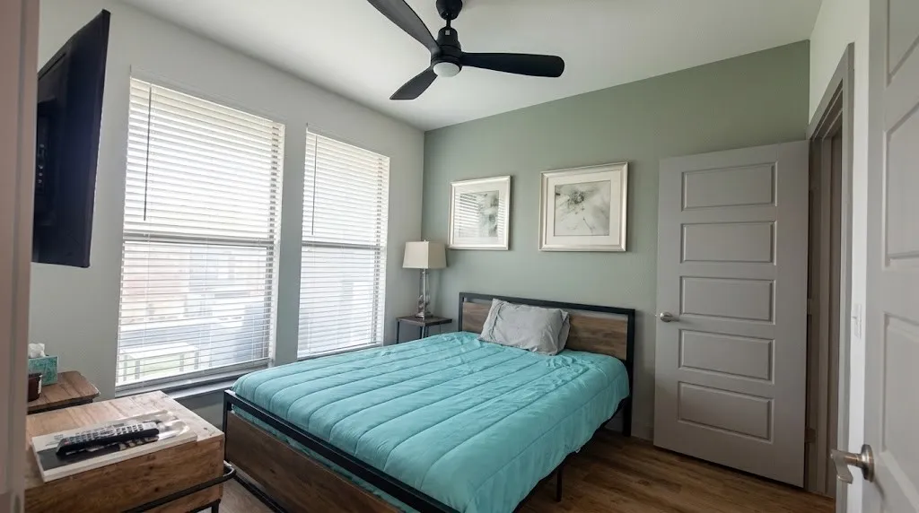 Two large windows with blinds, wood-finish flooring, a contemporary ceiling fan, and a paneled interior door