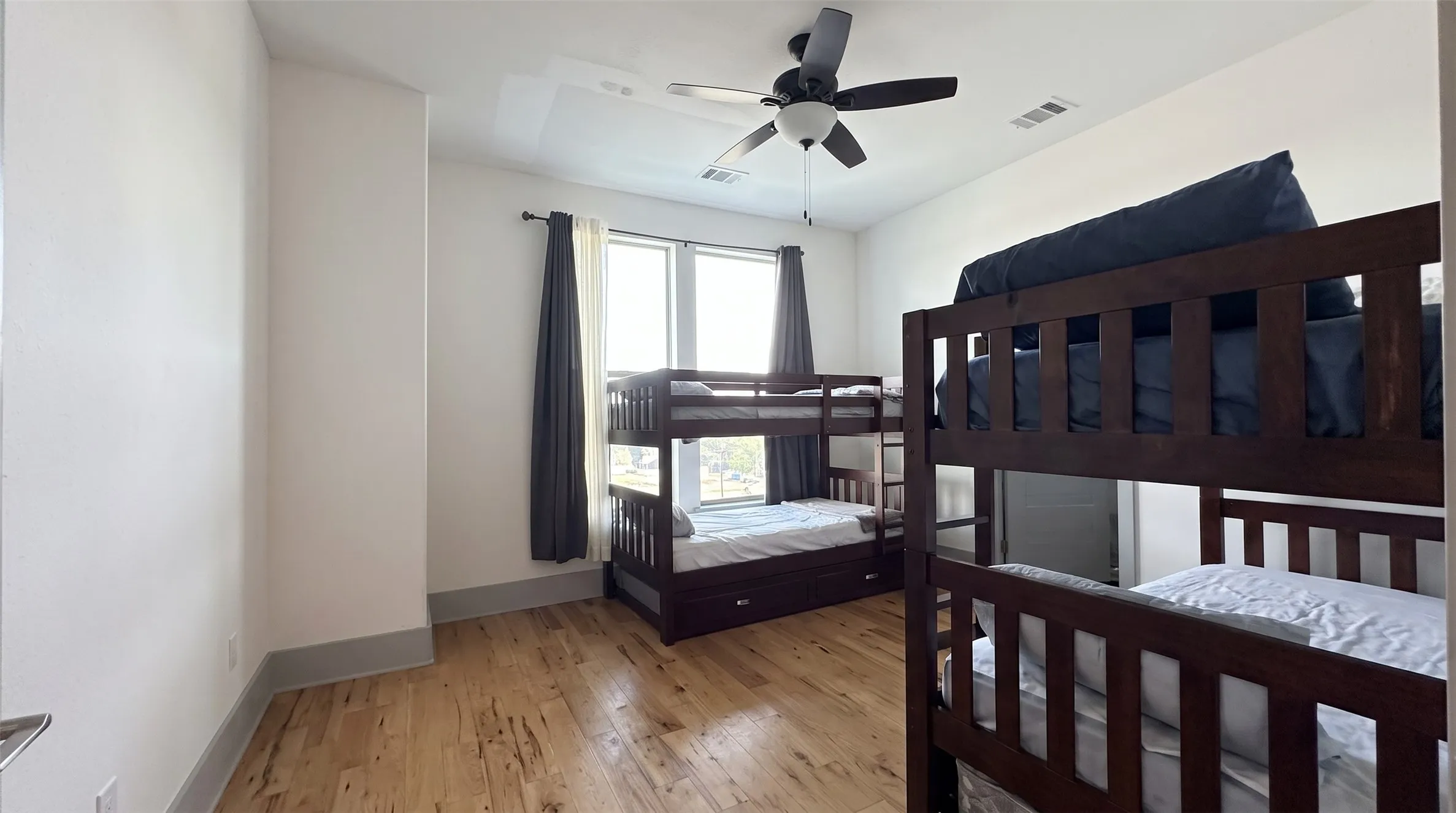 Wood-finish flooring throughout, ceiling fan, and two windows with dark drapery