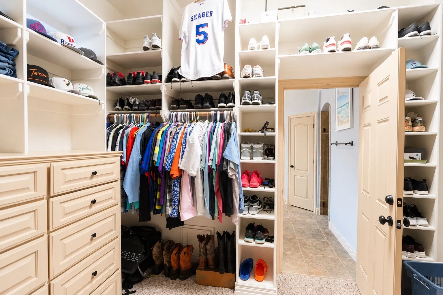 Custom closet system with built-in drawers, extensive shelving, hanging rods, and an open doorway leading to an interior space with tile flooring