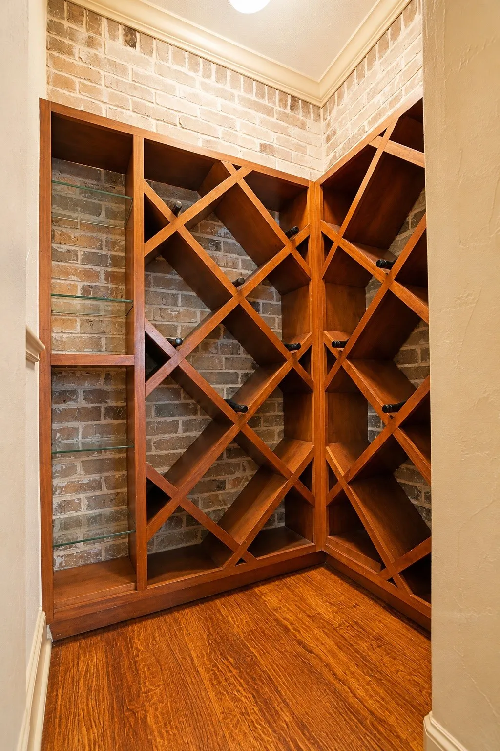 Built-in wood wine rack with diagonal storage, exposed brick wall, wood-finish flooring, and crown molding