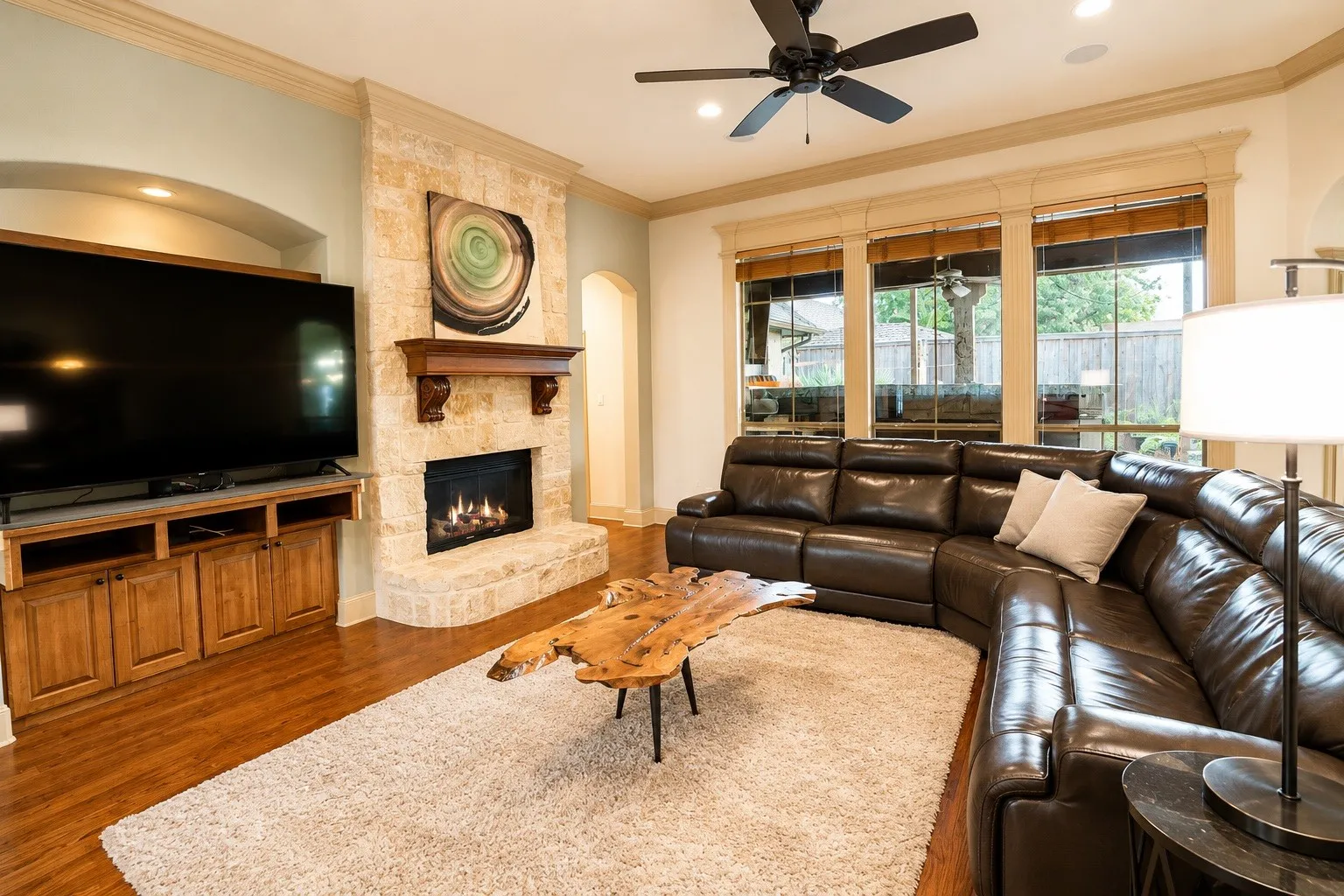 Stone-clad fireplace with a wood mantle, built-in media console with wood cabinetry, wood-finish flooring, crown molding, and large windows
