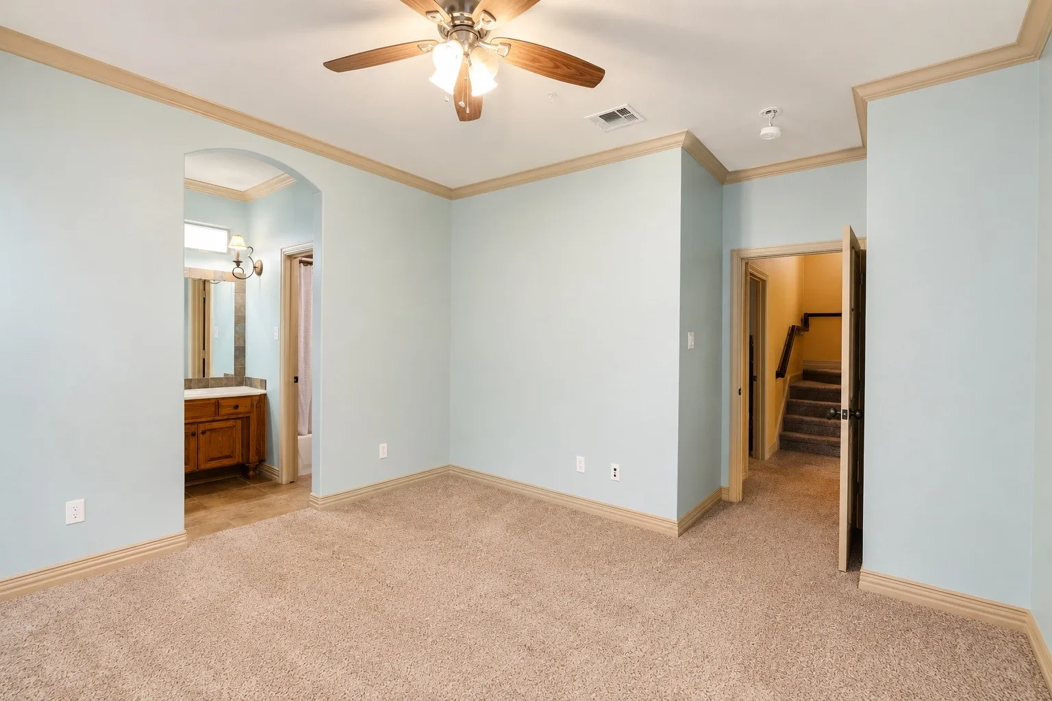 Carpeted flooring with crown molding, ceiling fan, and arched doorway leading to a vanity with a wood-finish cabinet