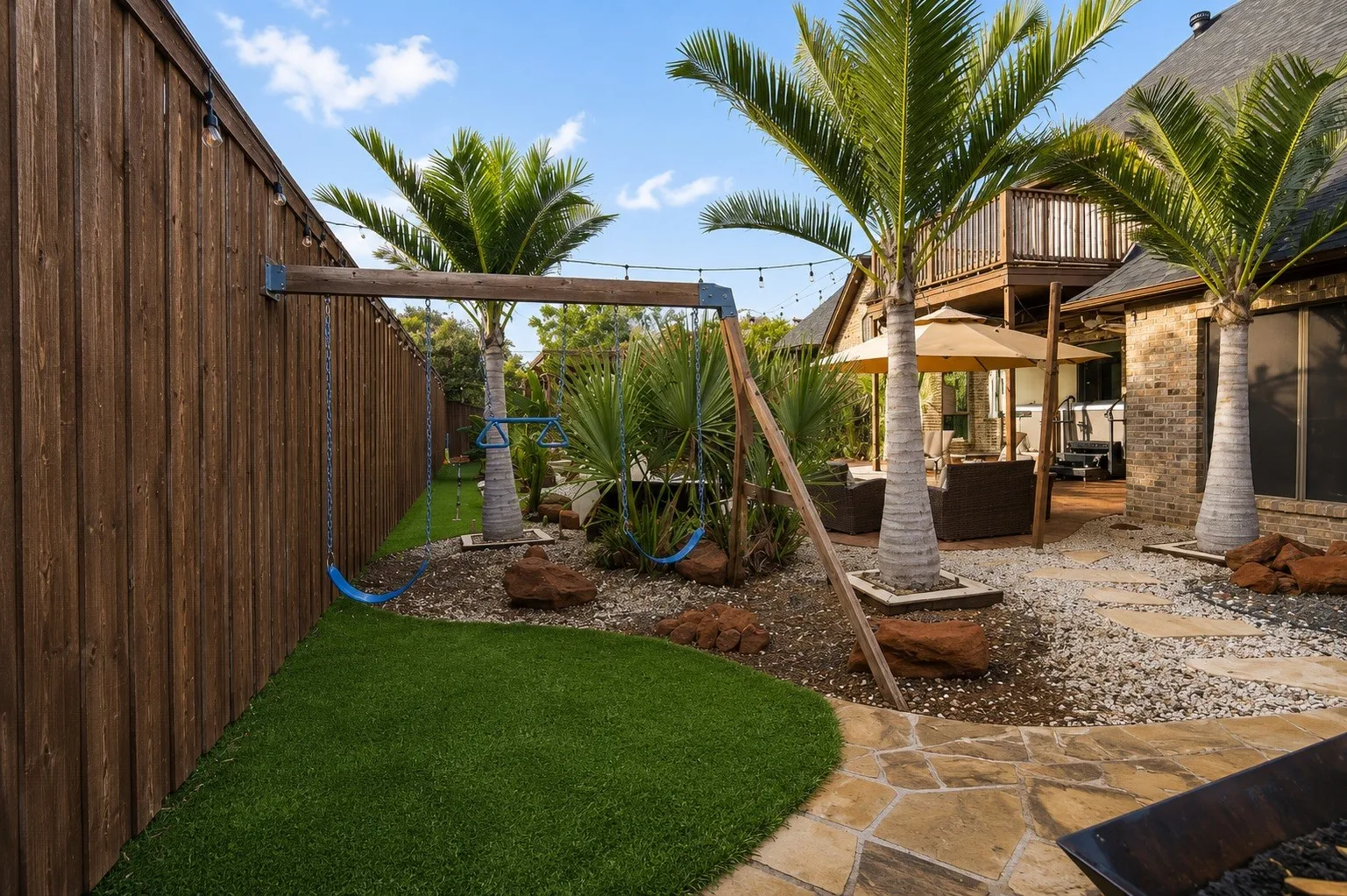Expansive backyard featuring a natural wood fence, artificial turf, flagstone patio, and mature palm trees