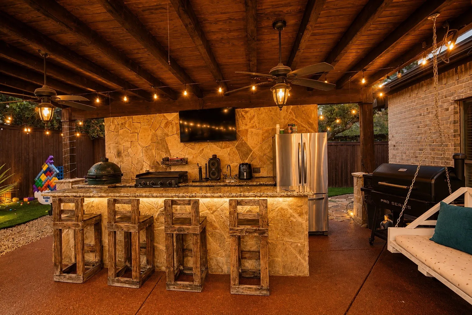 Covered outdoor kitchen featuring a stone-clad bar, built-in grill, and ceiling fans