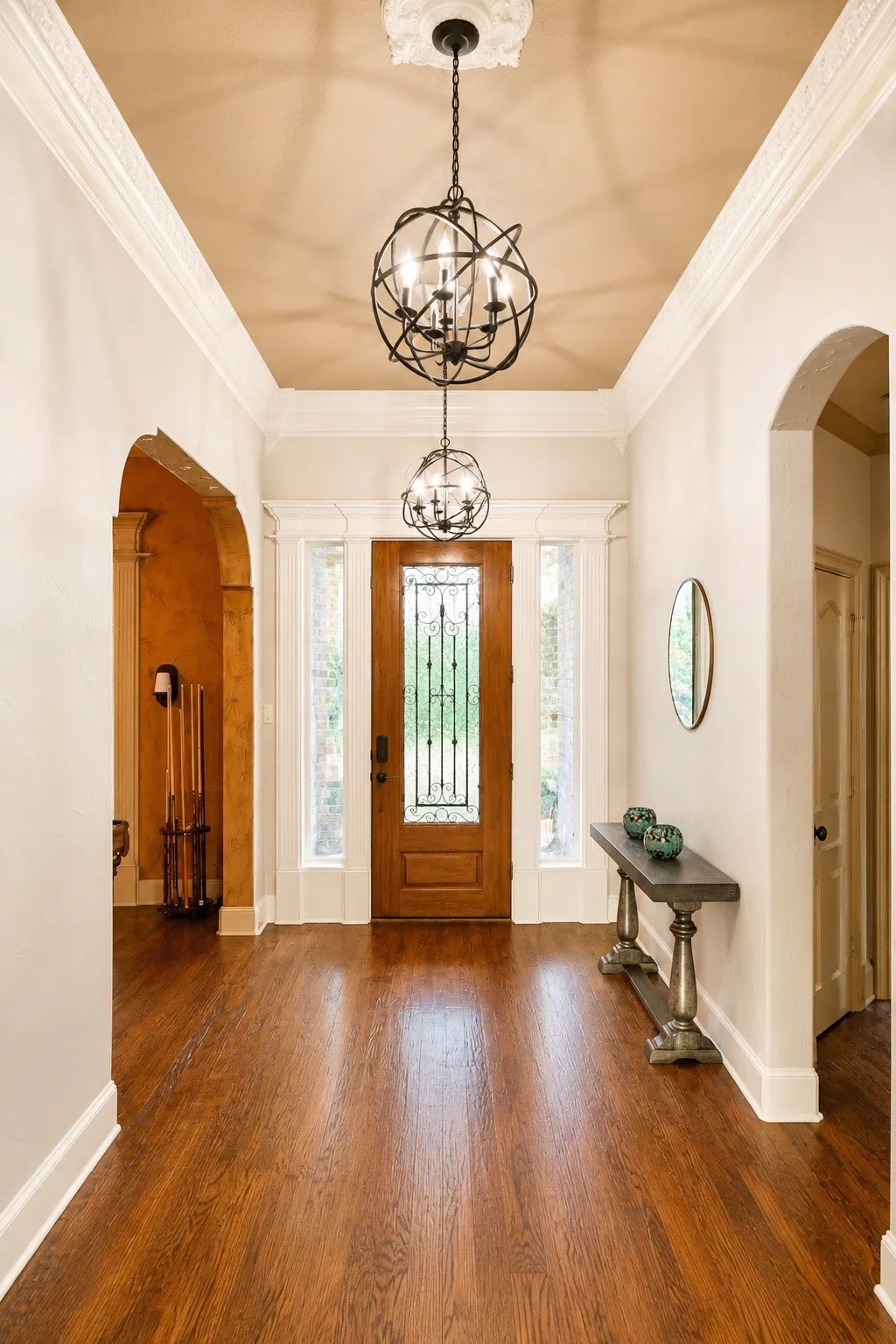Hardwood flooring, arched doorways, decorative light fixtures, coffered ceiling, and a paneled entry door