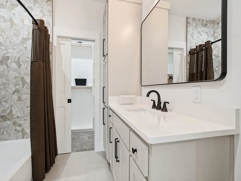 Vanity with white countertop and integrated sink, black framed mirror, black faucet, and white cabinetry with black hardware