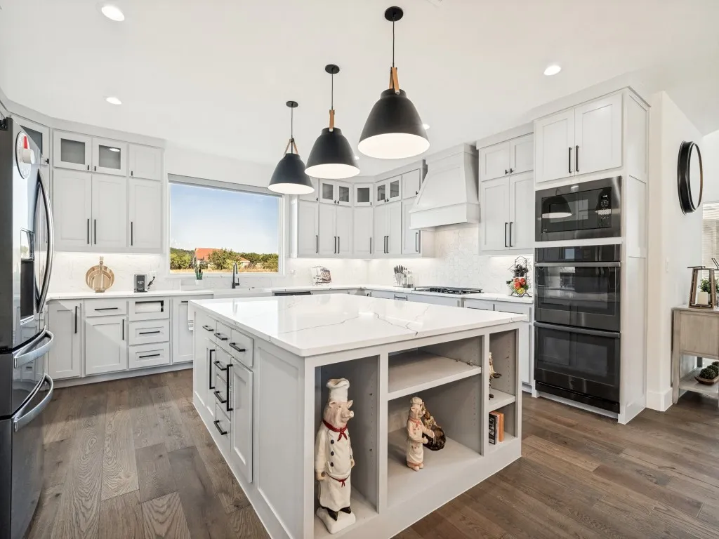 Kitchen featuring wood-finish flooring, light-toned cabinetry, a spacious center island with a white countertop, and built-in double ovens
