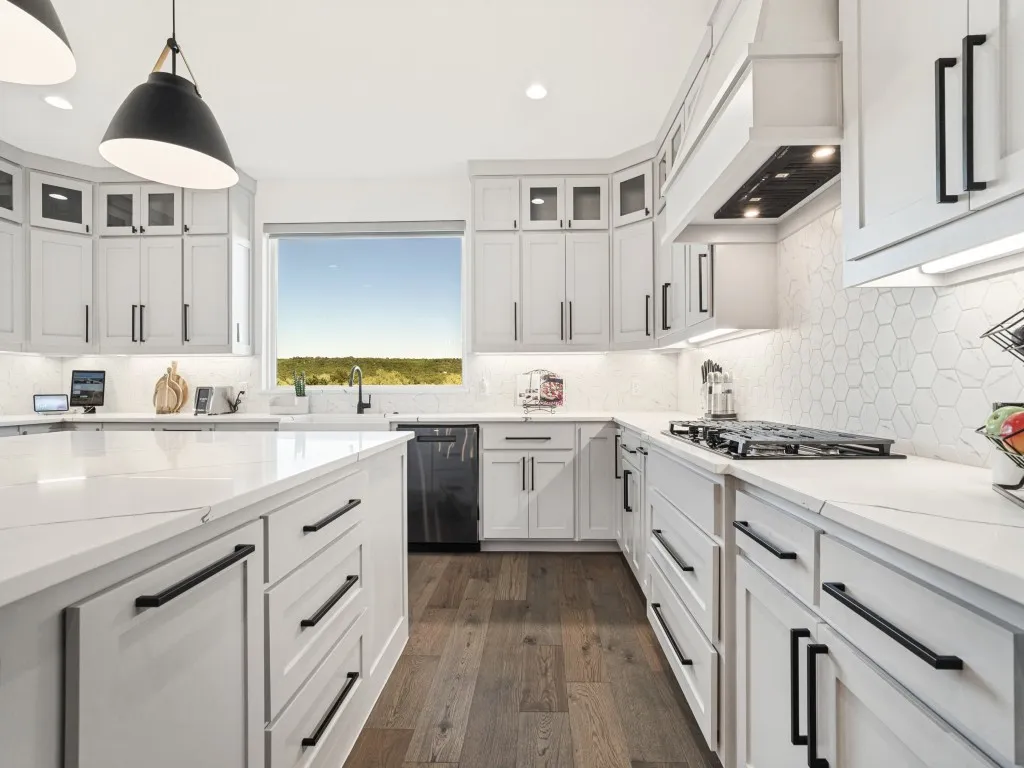 White cabinetry with matte black hardware, light-toned countertops, and a hexagonal tile backsplash