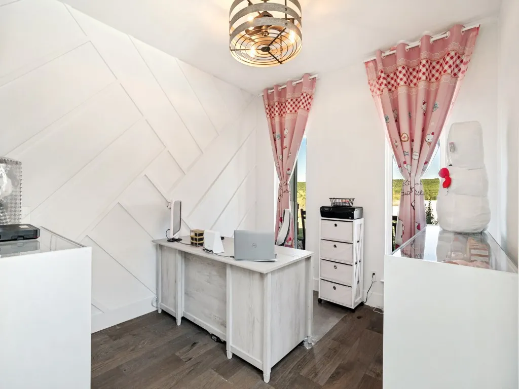 Feature wall with geometric paneling, two windows providing natural light, a contemporary ceiling light fixture, and wood-finish flooring