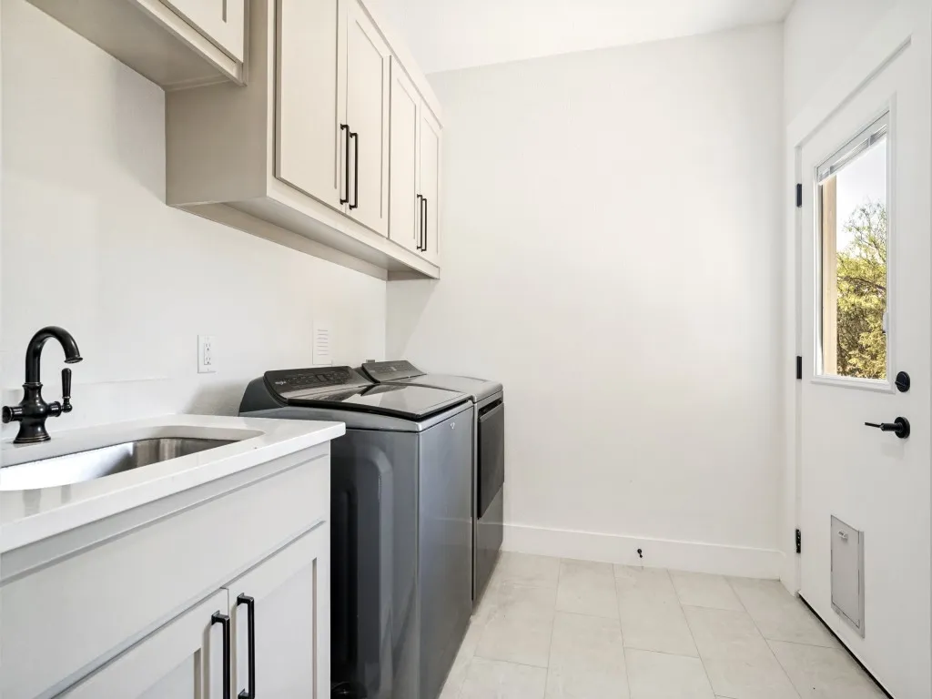 Utility room featuring light-toned cabinetry, a stainless steel sink with a dark-finish faucet, and light-toned tile flooring