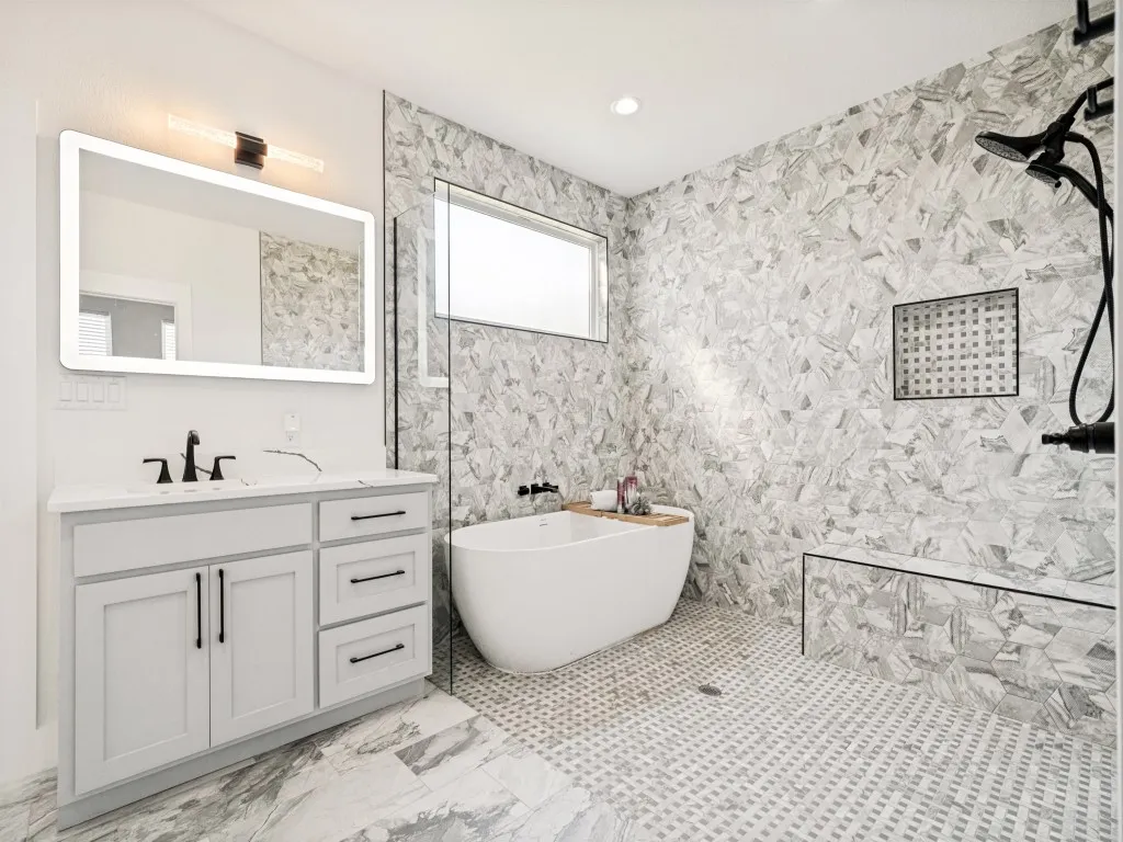 Modern bathroom featuring a freestanding tub, walk-in shower with a built-in bench, white vanity with ample storage, and a backlit mirror