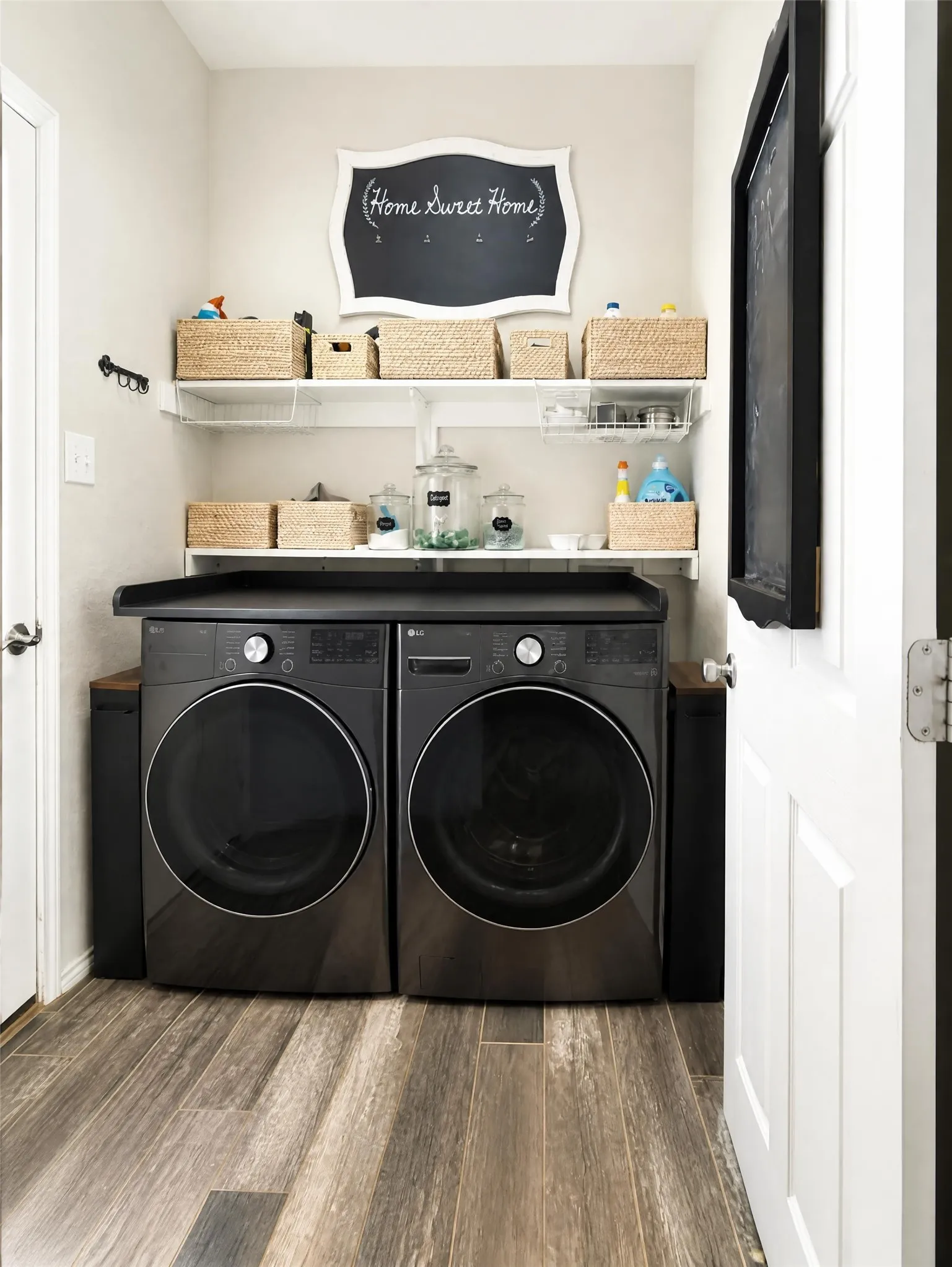 Laundry area with wood-finish flooring, two large appliances, a dark countertop, and open shelving
