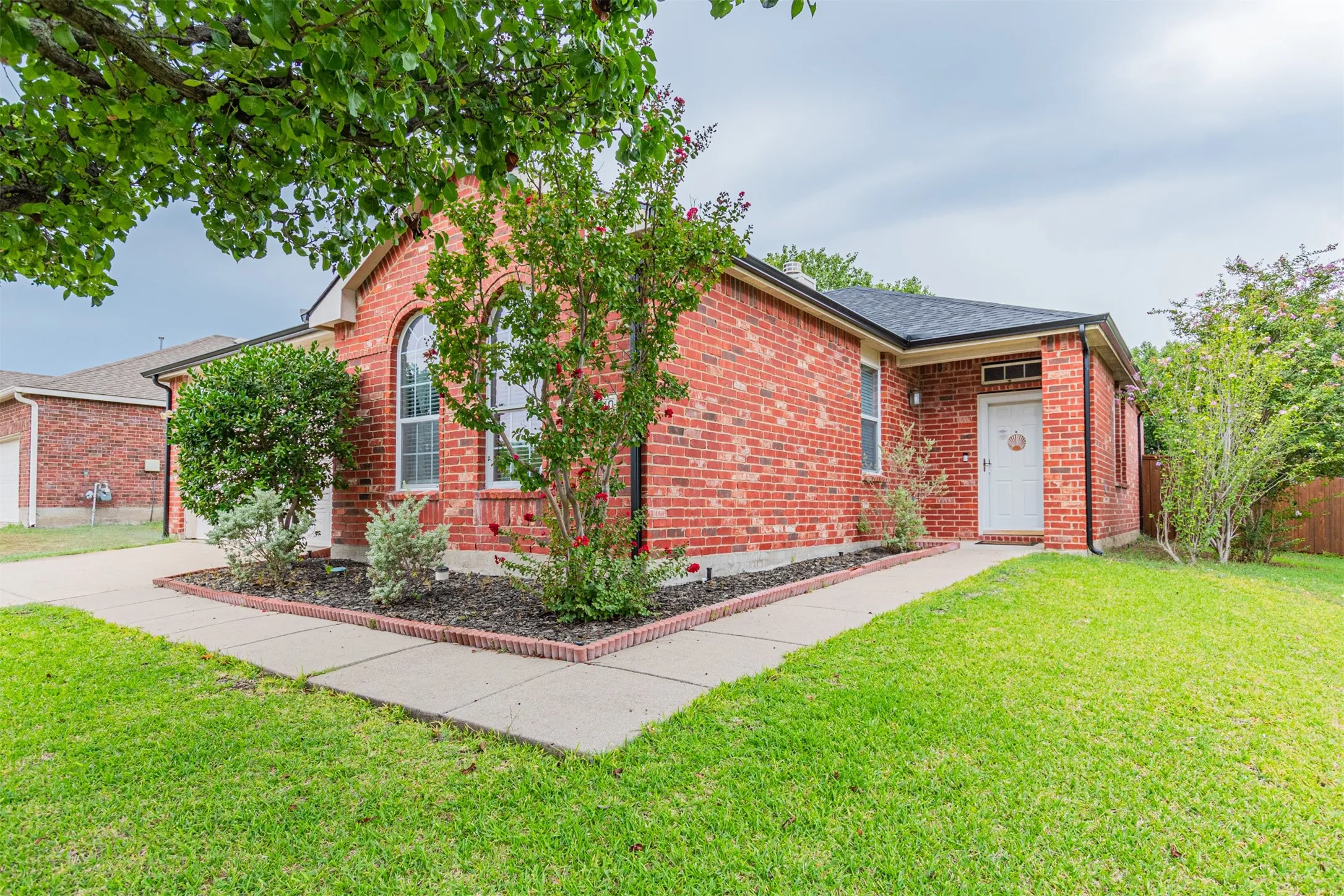 Red brick exterior featuring a covered entry, arched window, and landscaped beds