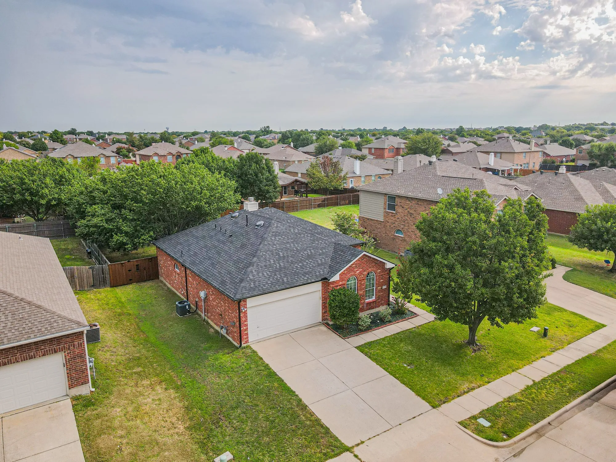Brick exterior, attached two-car garage, concrete driveway, mature trees, and a shingle roof