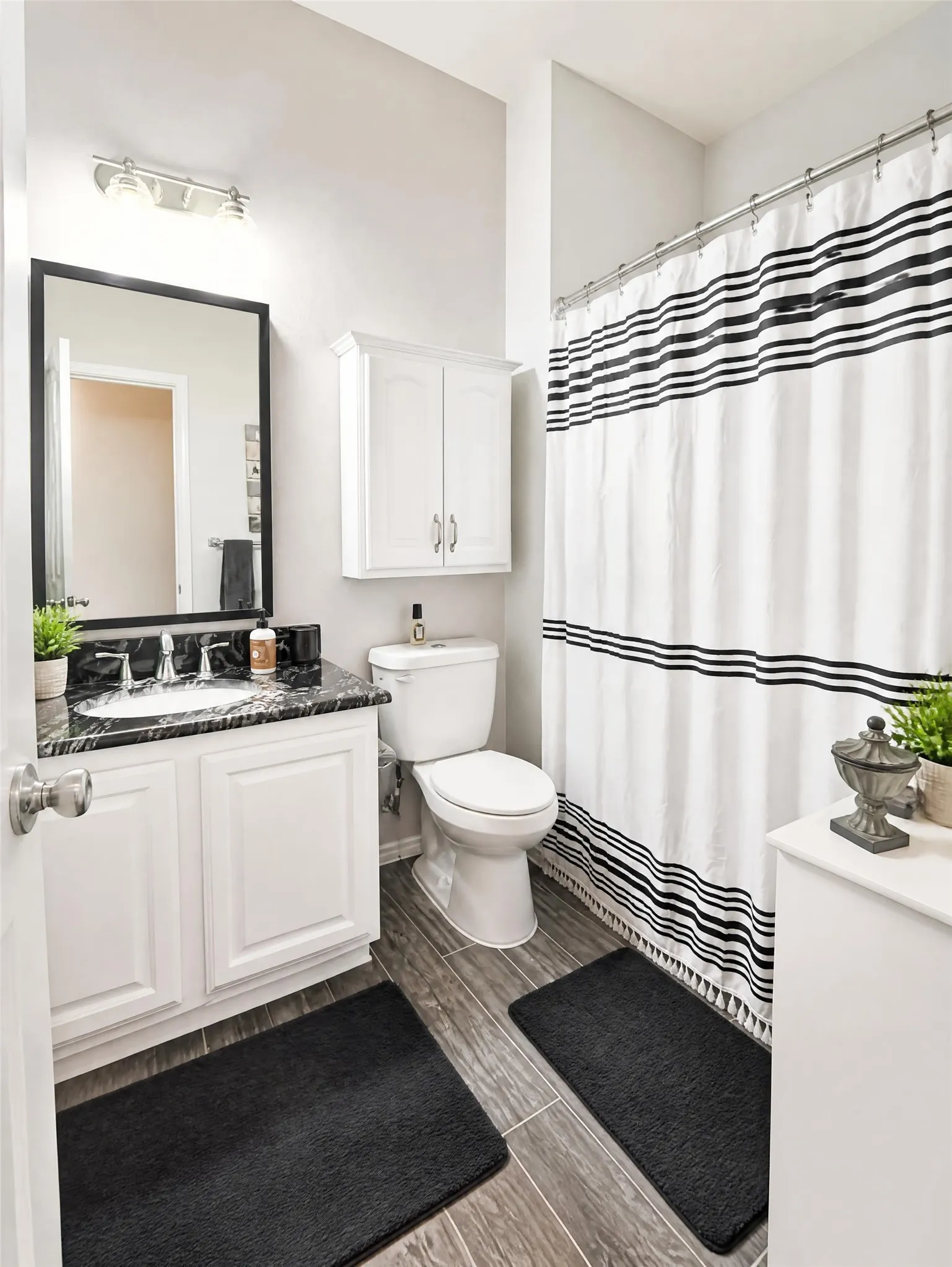 Bathroom featuring a single vanity with dark countertop, white cabinetry, integrated sink, and wood-finish flooring