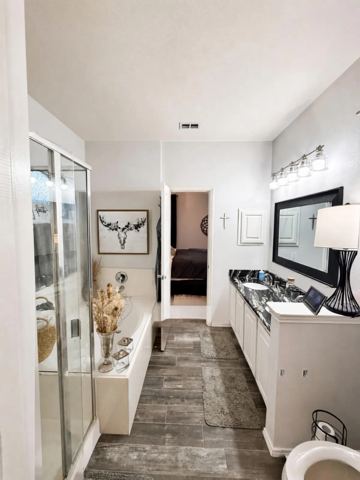 Wood-finish flooring, built-in bathtub, glass-enclosed shower, dual vanity with undermount sinks, and dark stone countertop