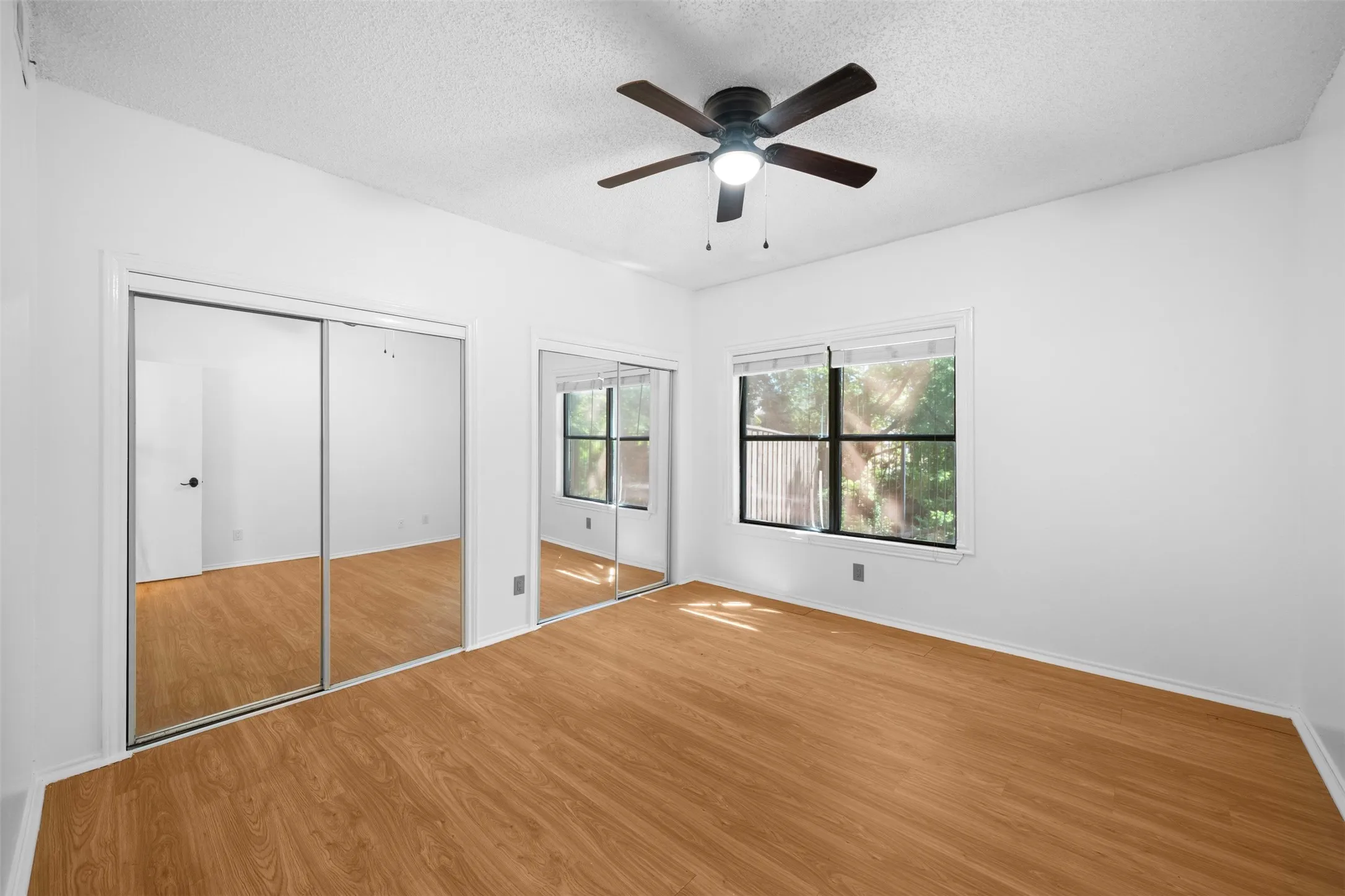 Wood-finish flooring, mirrored sliding closet doors, ceiling fan with light, and dual windows