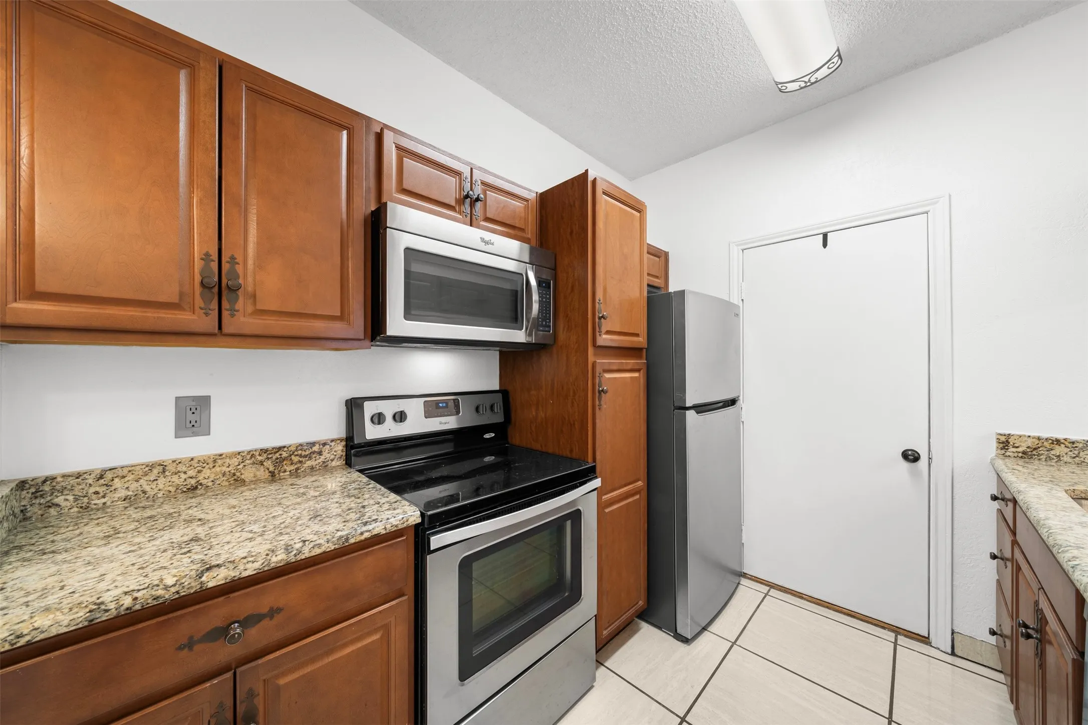 Kitchen featuring wood cabinetry, stainless steel appliances, speckled countertops, and tile flooring