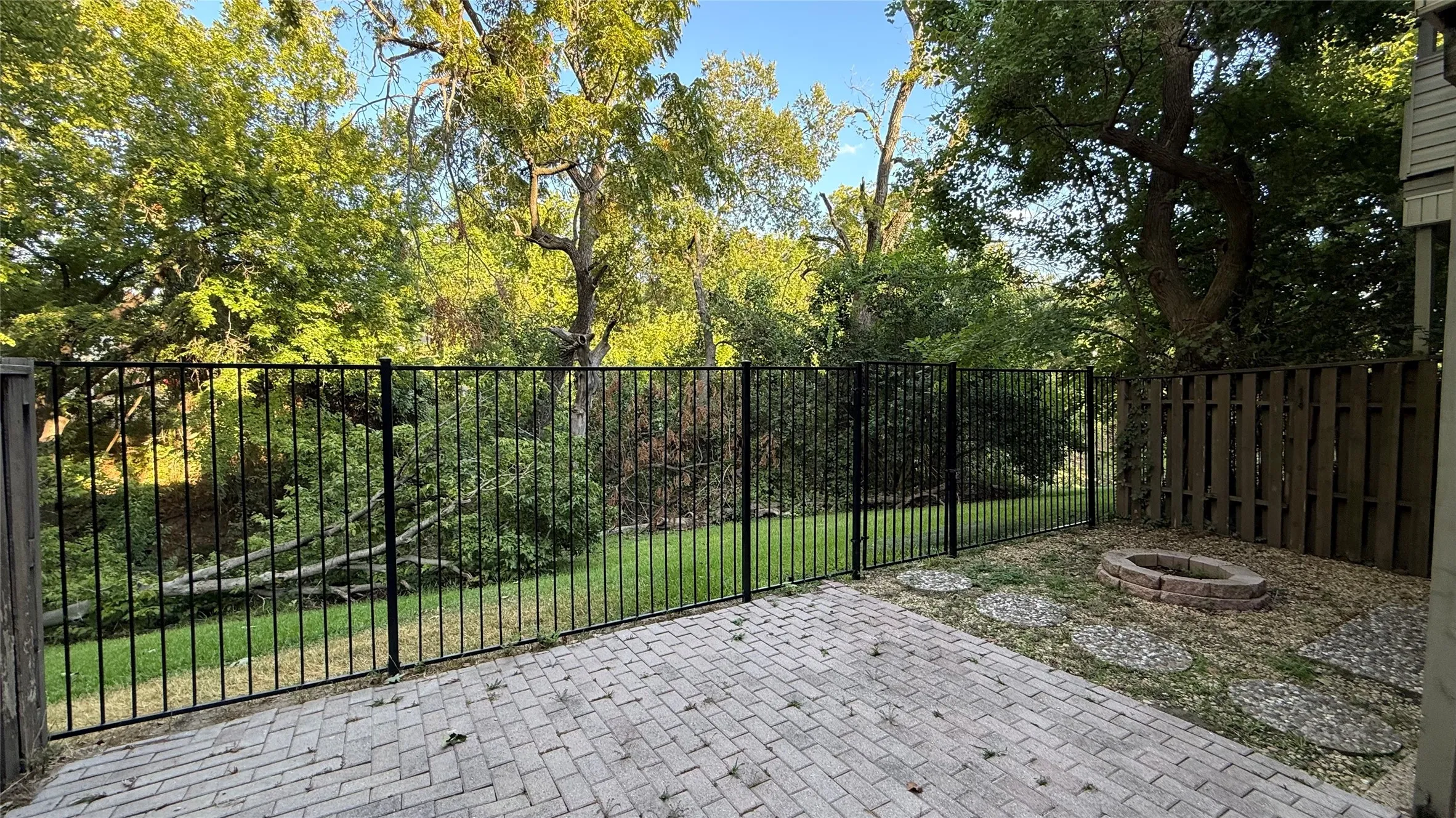 Outdoor patio featuring paver stones, a black metal fence, a wood fence, a fire pit, and stone pavers