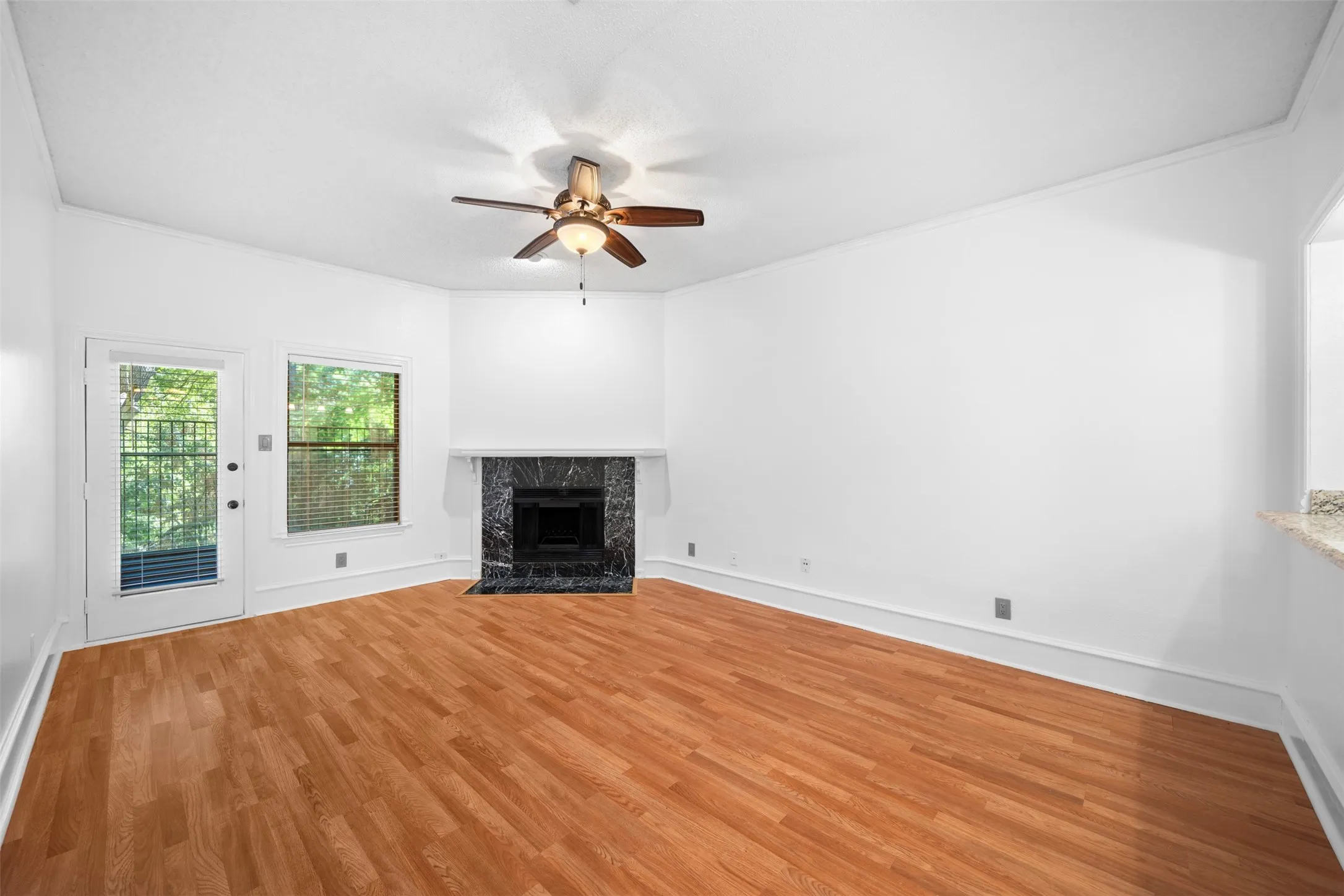 Wood-finish flooring, corner fireplace with a dark stone surround, white walls, and a ceiling fan