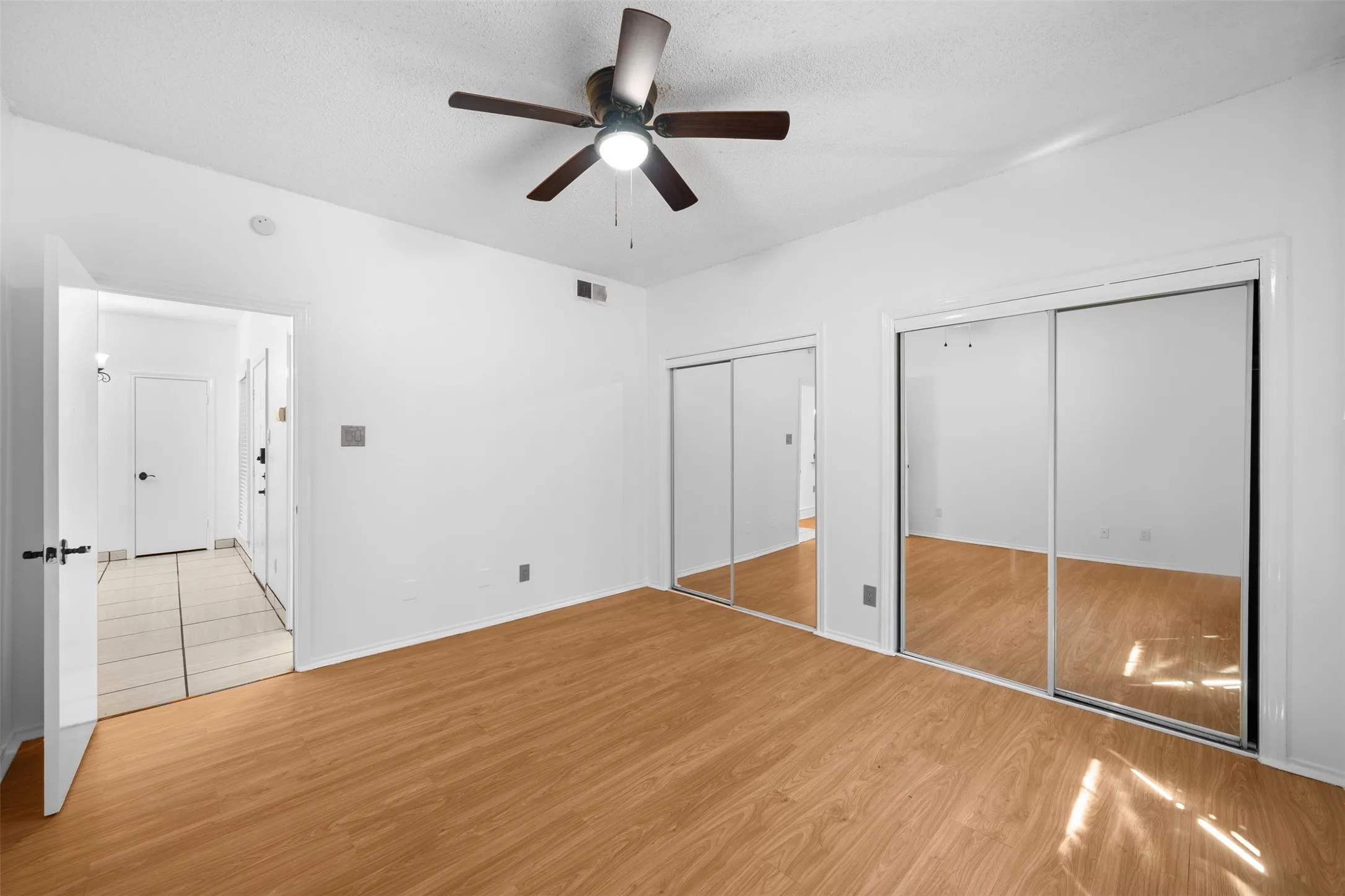 Wood-finish flooring, ceiling fan with integrated lighting, and mirrored sliding closet doors