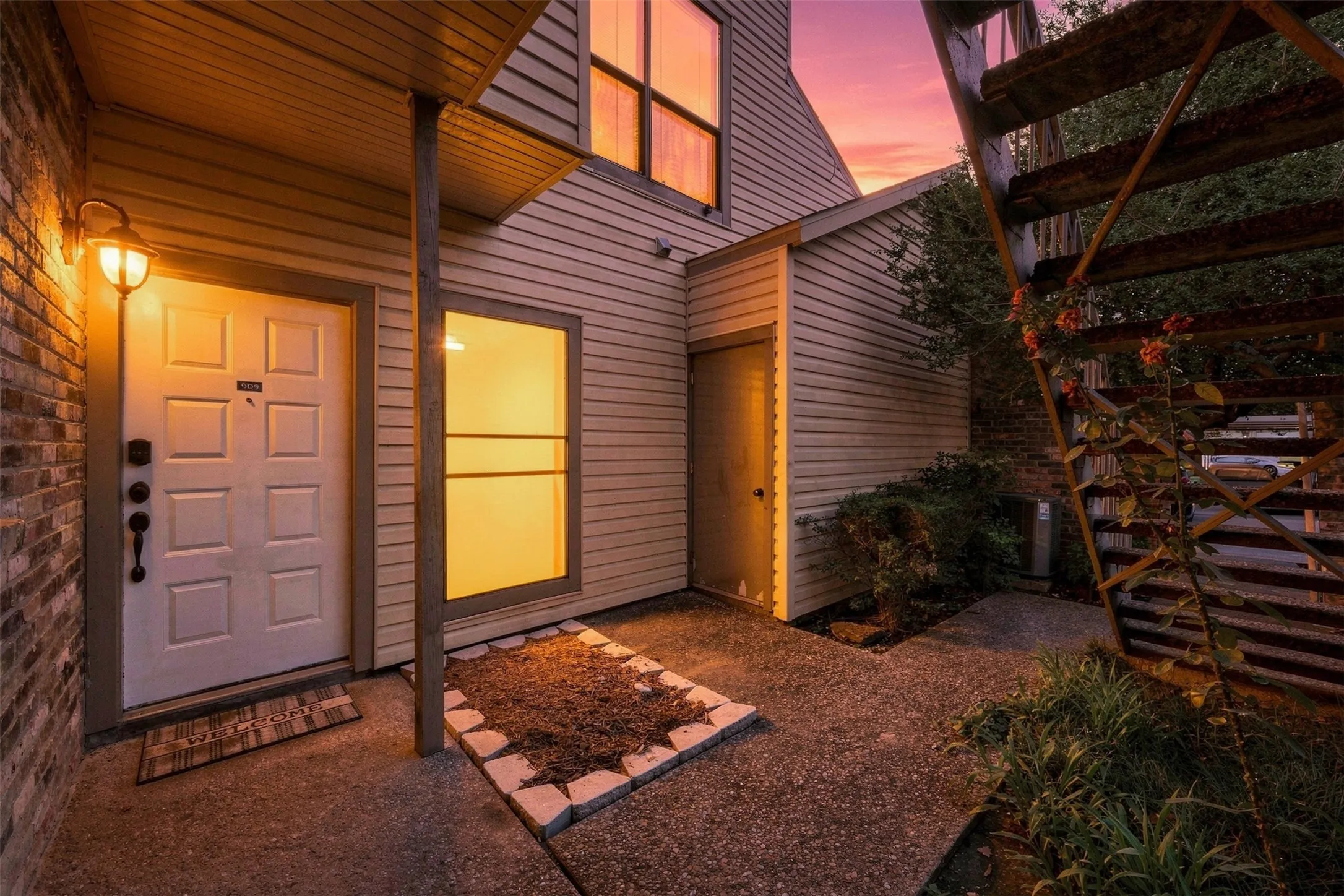 Brick and siding exterior with a paneled entry door, an exterior wall sconce, and an adjacent built-in storage unit