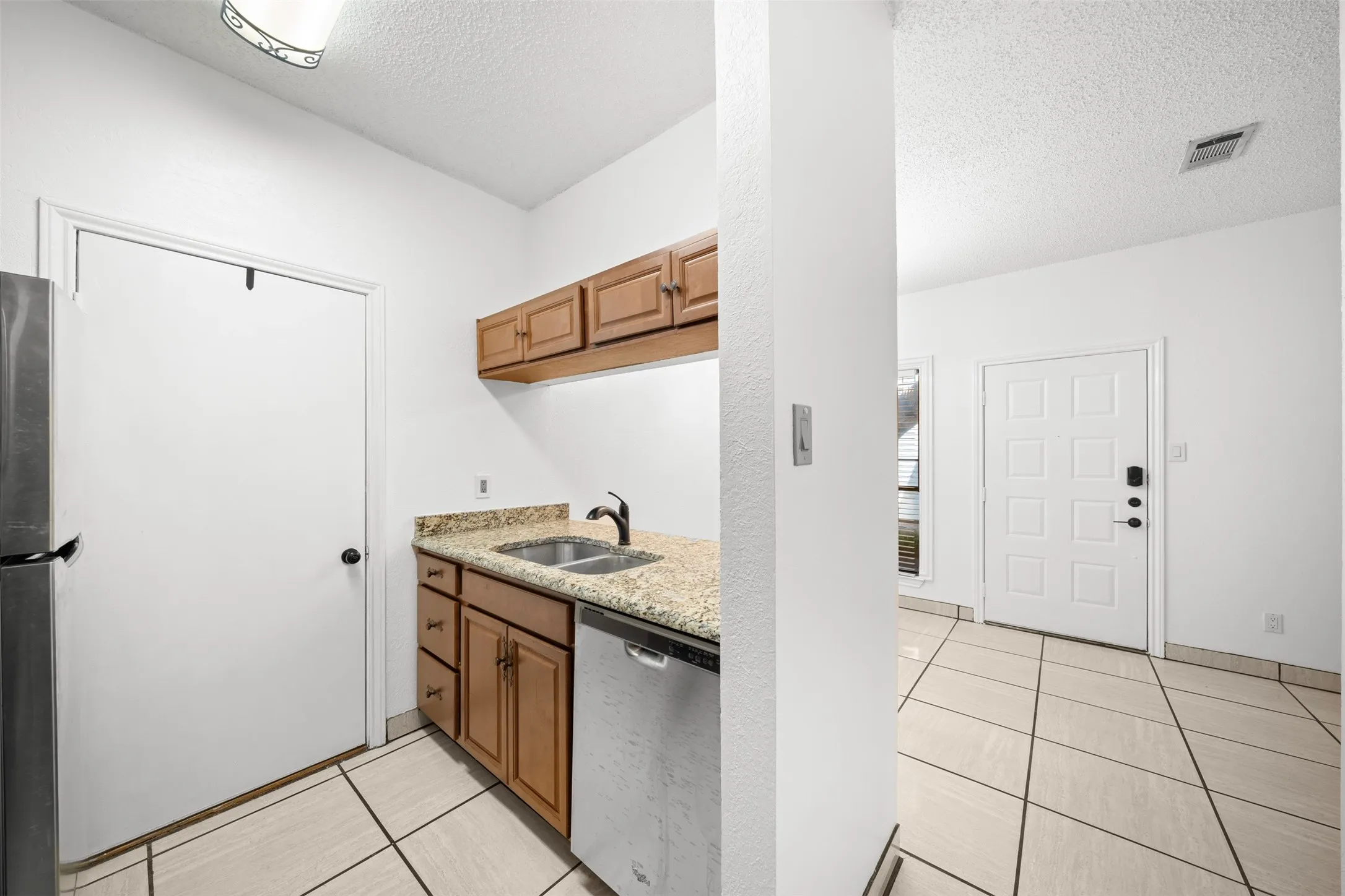 Kitchenette featuring wood cabinetry, stone-finish countertops, stainless steel sink, and integrated dishwasher