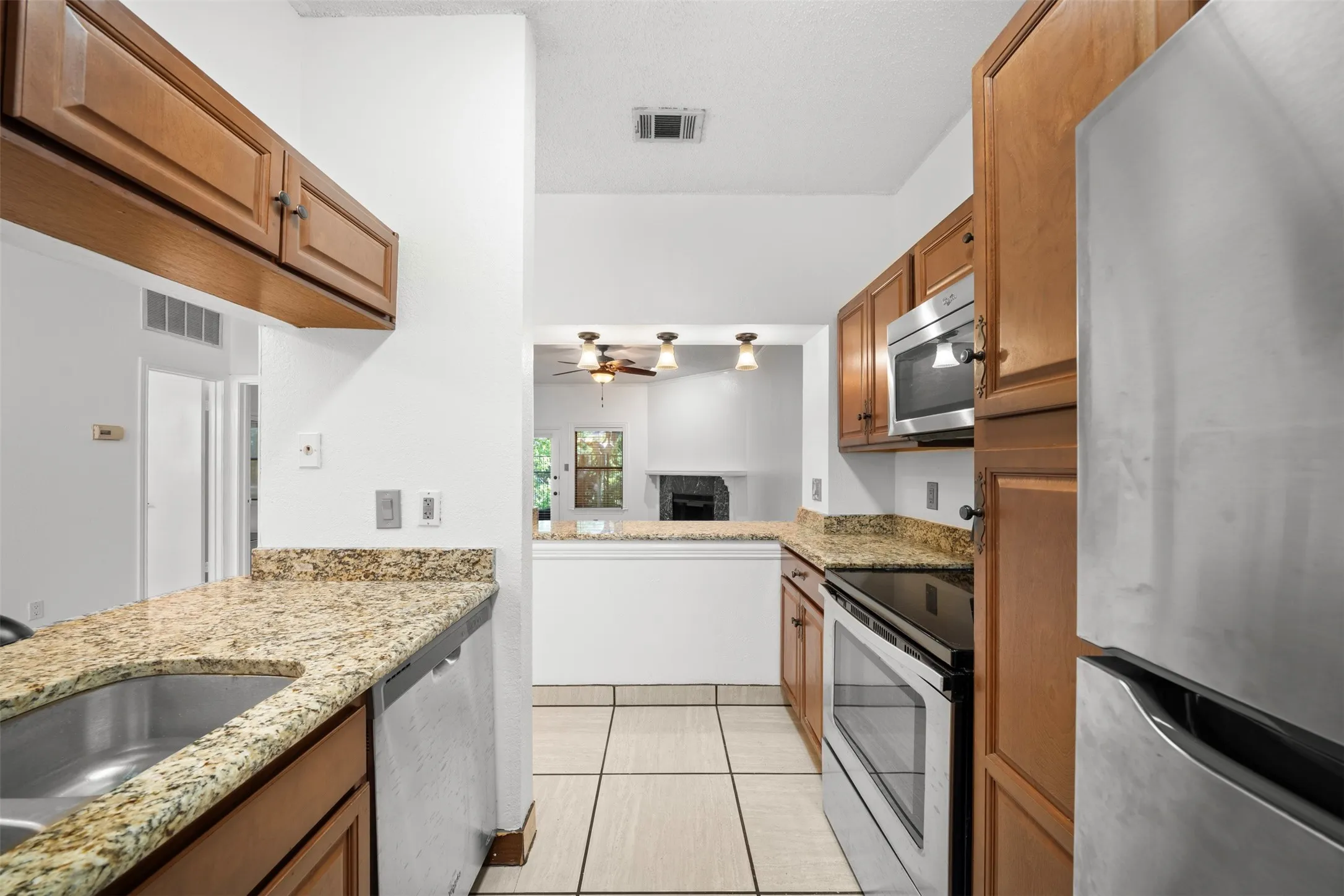 Kitchen featuring wood cabinetry, stainless steel appliances, granite countertops, and tiled flooring