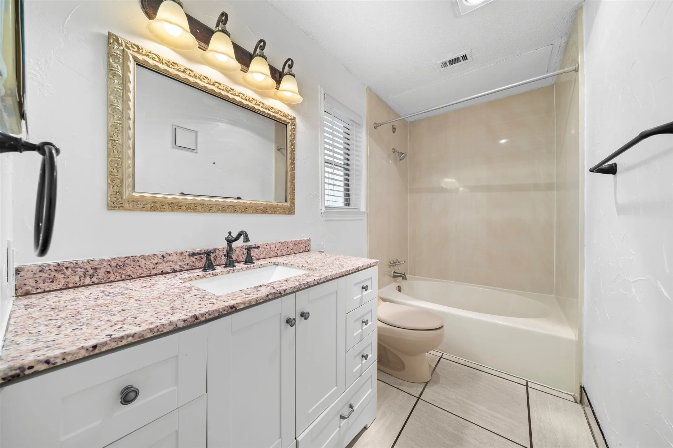 White shaker-style vanity with a speckled countertop, undermount sink, and dark-toned faucet