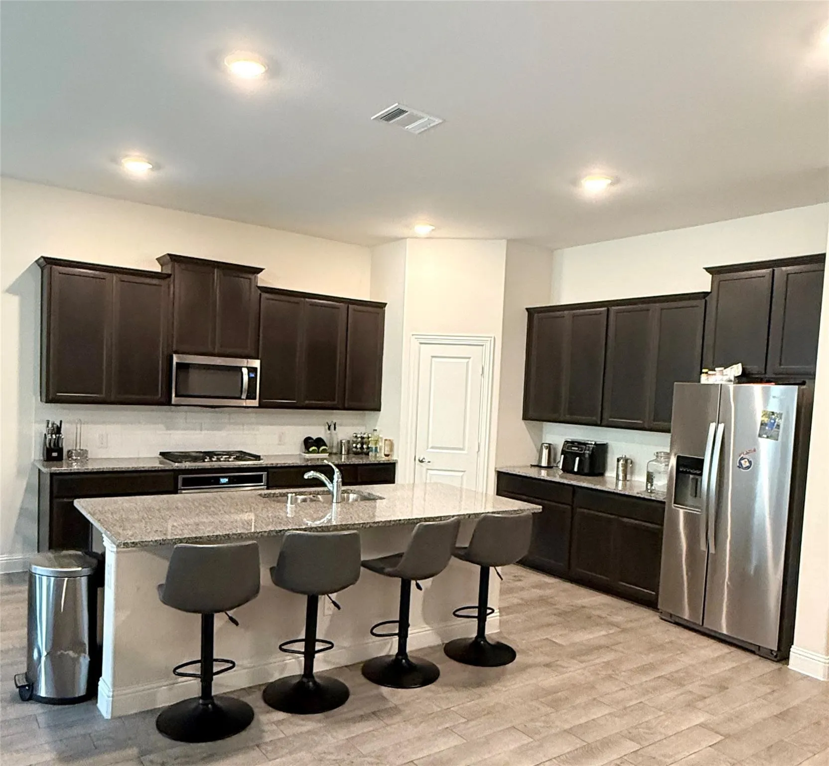 Kitchen featuring dark wood-finish cabinetry, light-colored countertops, stainless steel appliances, a center island with a sink, and wood-finish flooring