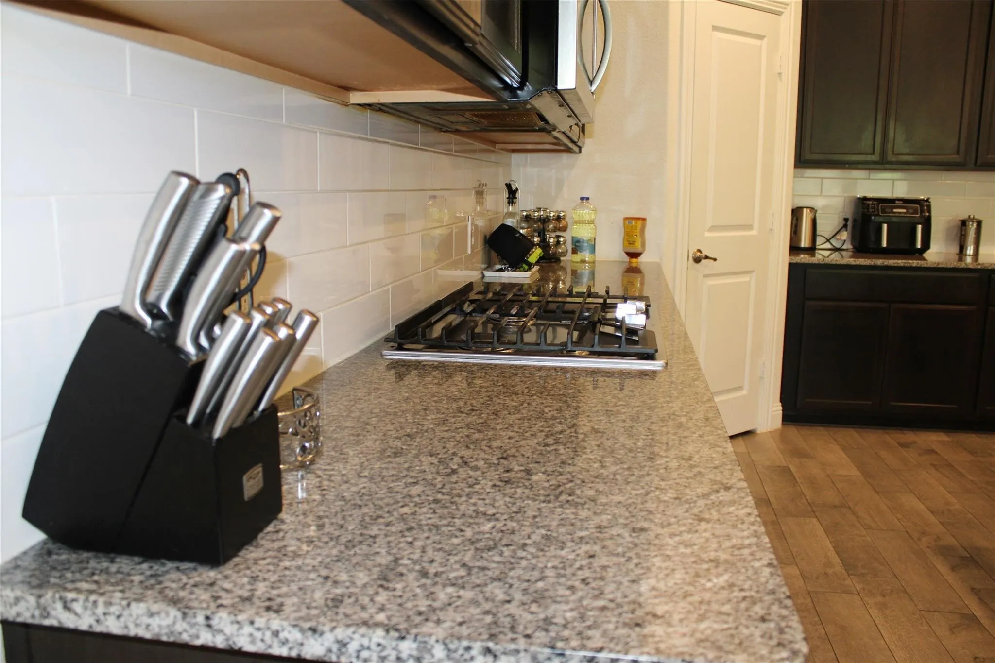 Granite-style countertop, white subway tile backsplash, gas range, wood-finish flooring, and dark wood cabinetry