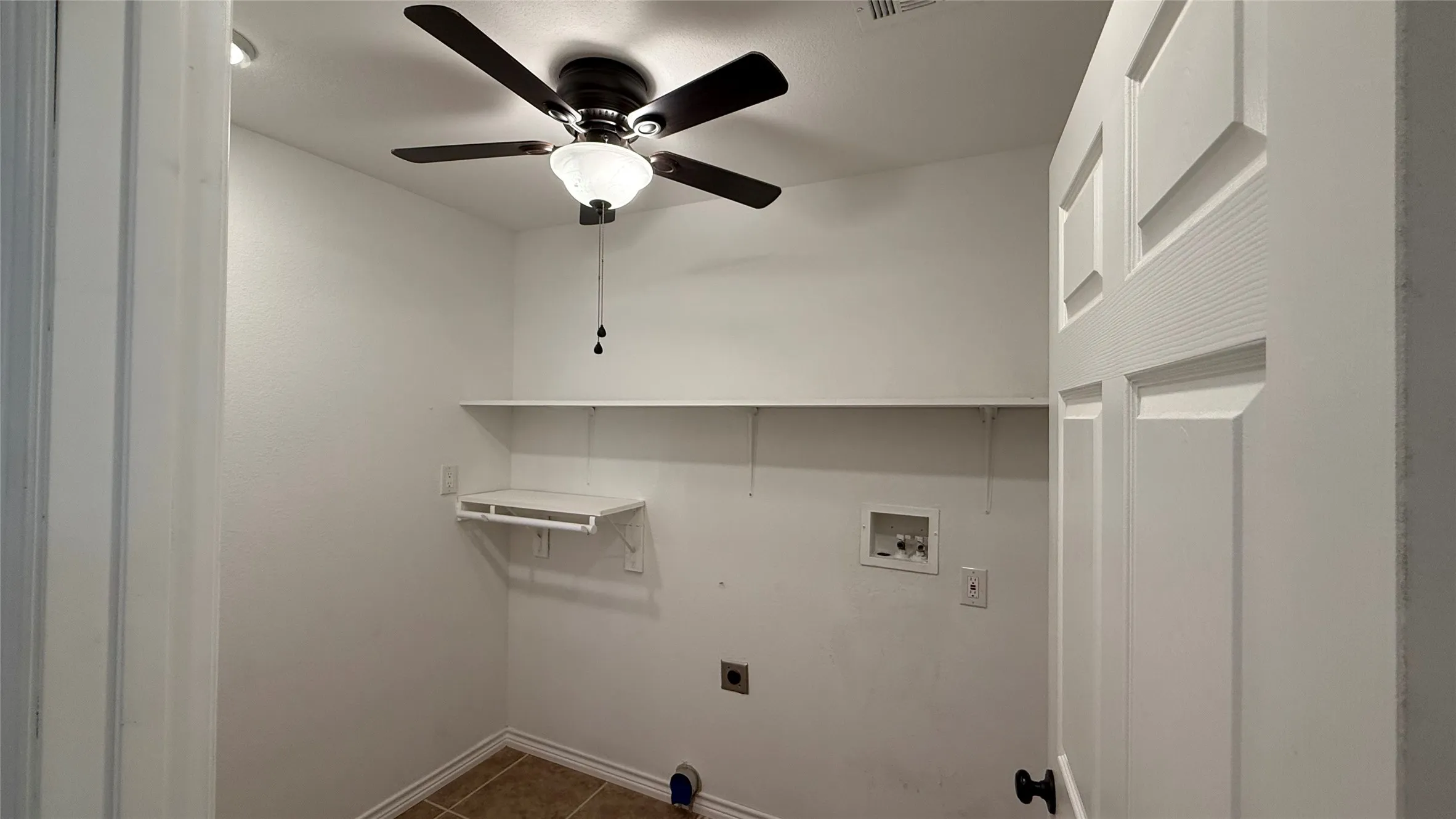 Utility room featuring a ceiling fan with integrated lighting, wall-mounted shelving, and tile flooring