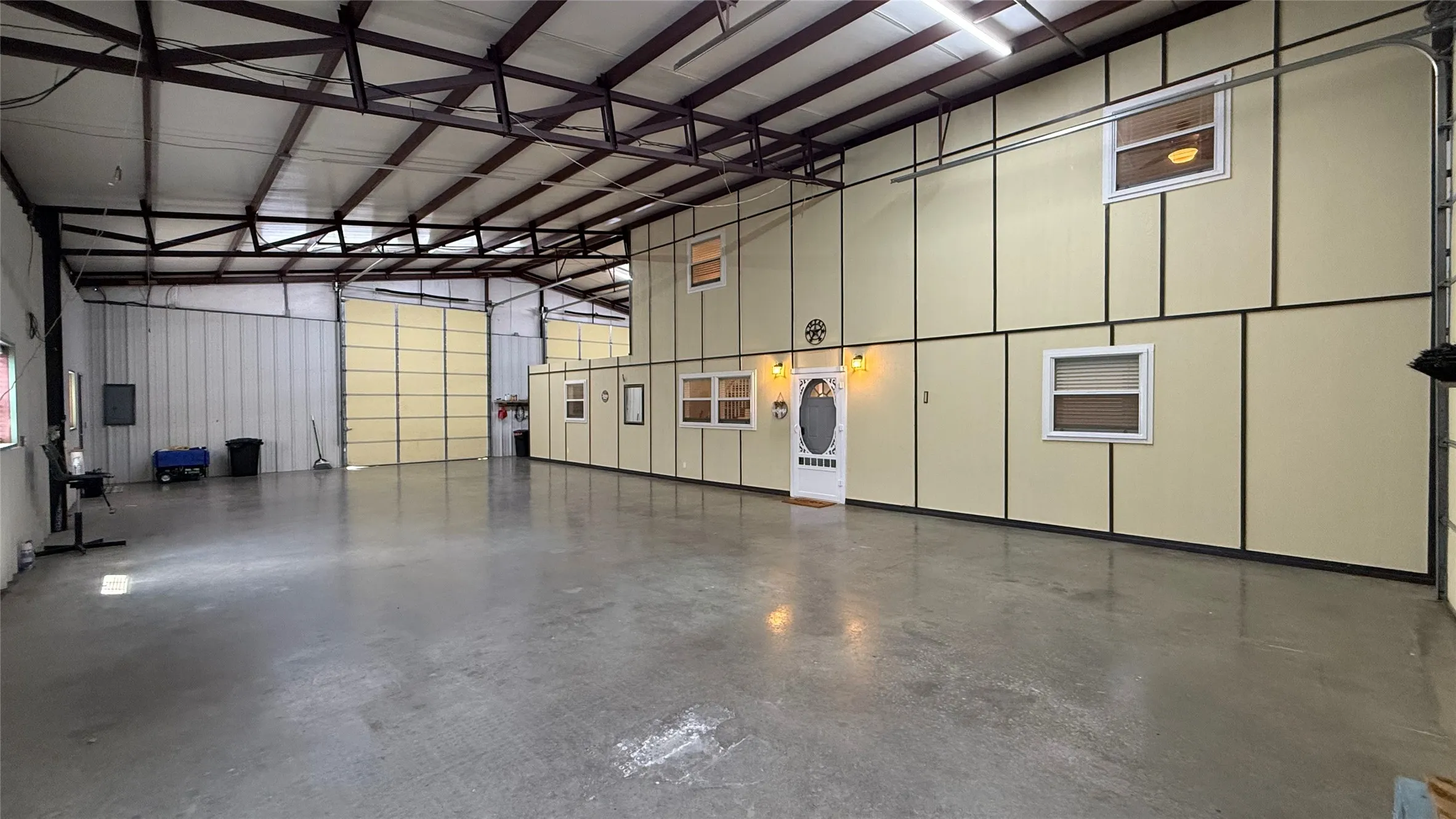 Expansive warehouse space featuring concrete flooring, exposed structural steel beams, multiple roll-up doors, and interior paneled walls with integrated windows
