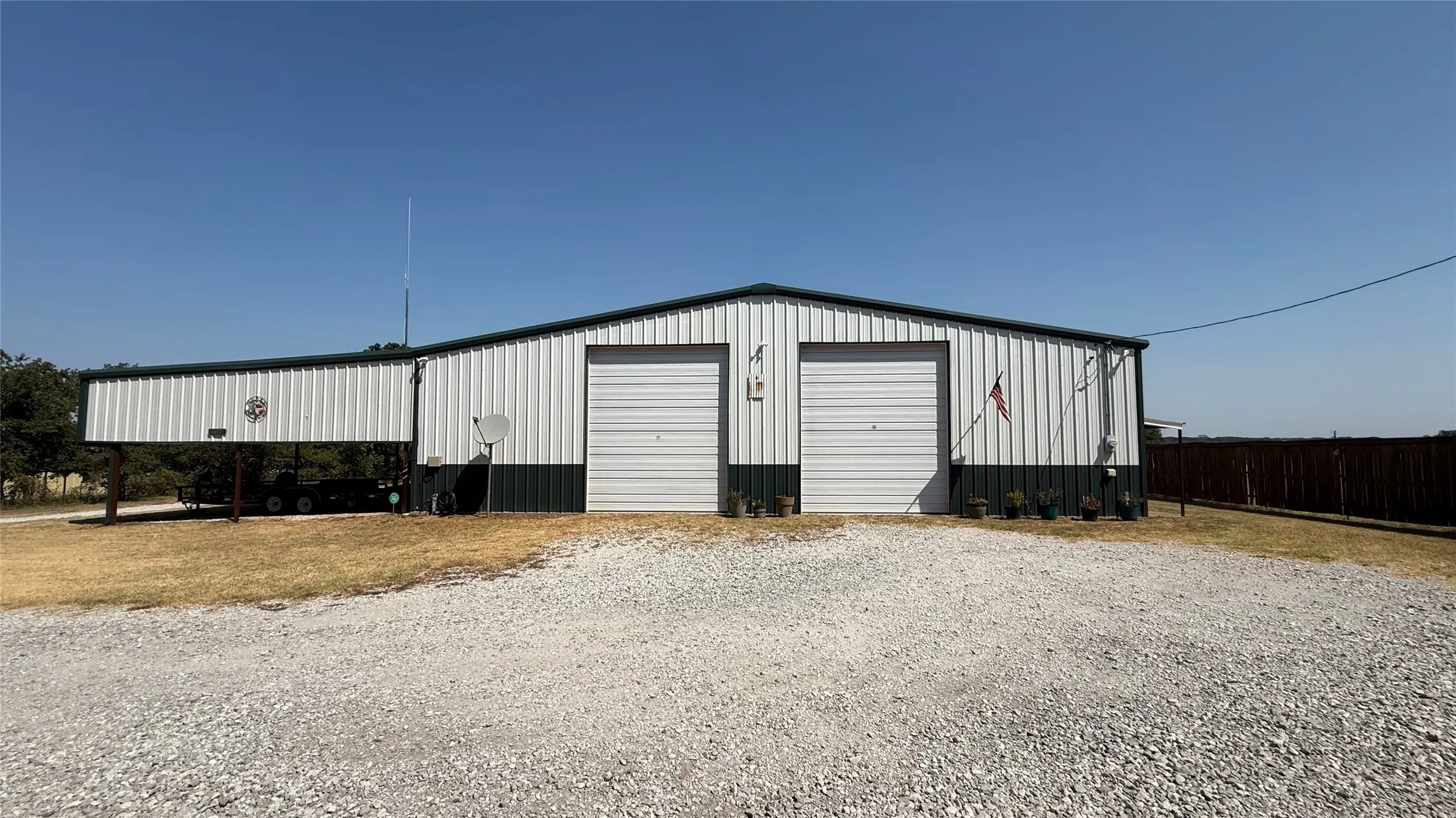 Metal building featuring two roll-up garage doors, an extended covered carport, and a gravel drive