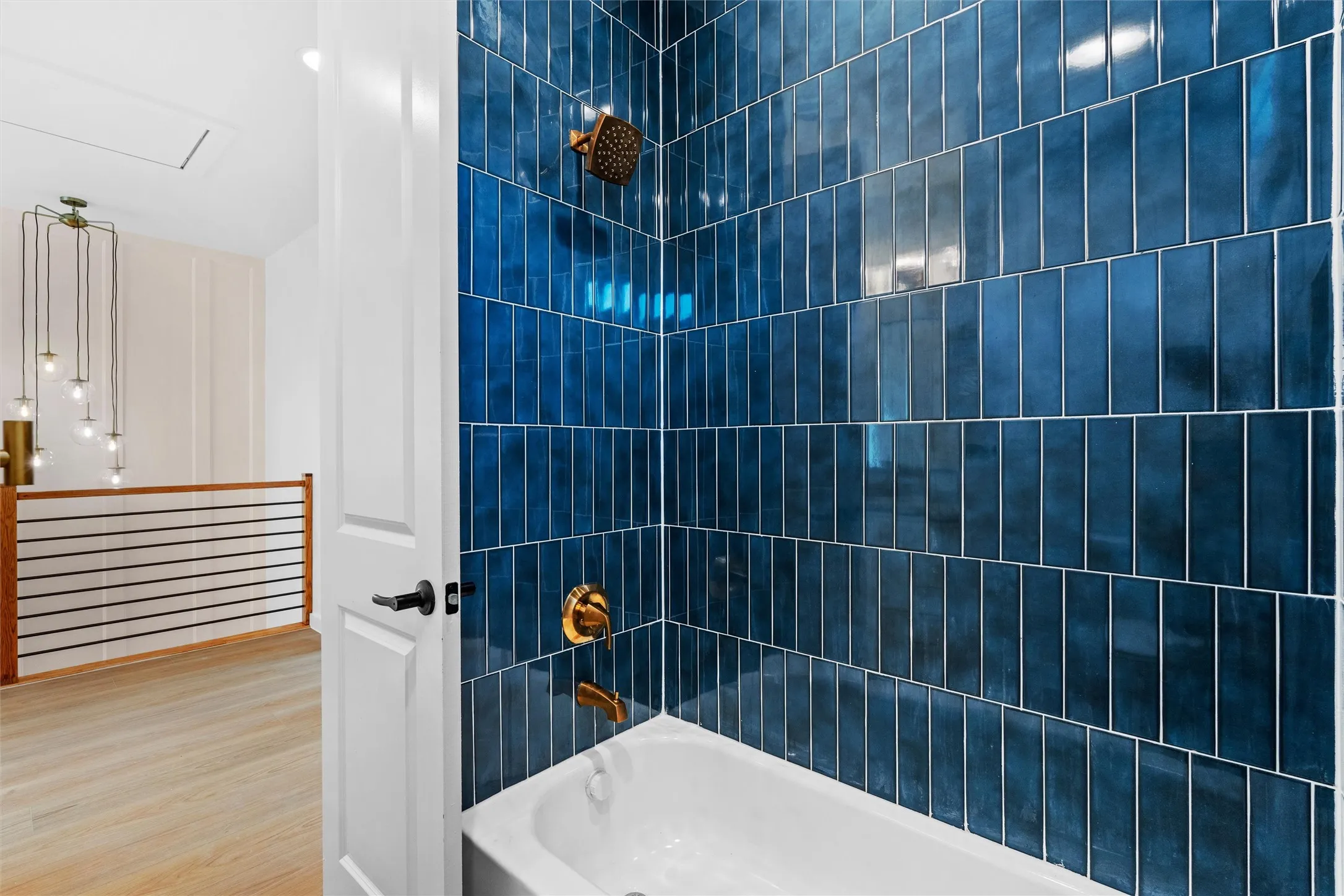 Bathroom featuring a white bathtub, blue vertical subway tile surround, and gold-finish fixtures