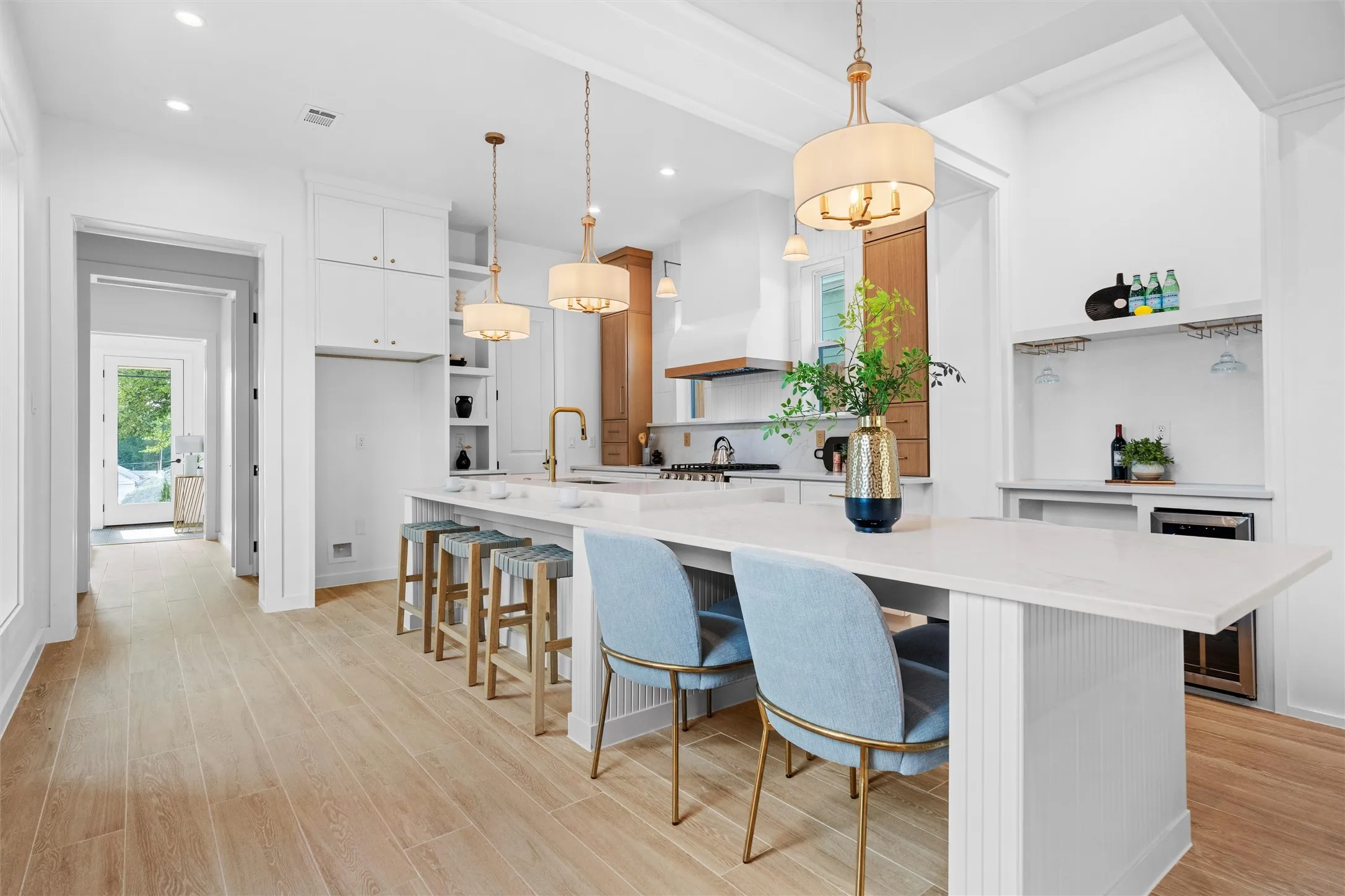 Open-concept kitchen featuring an oversized island with seating, pendant lighting, wood-finish flooring, white cabinetry, and a dedicated beverage station