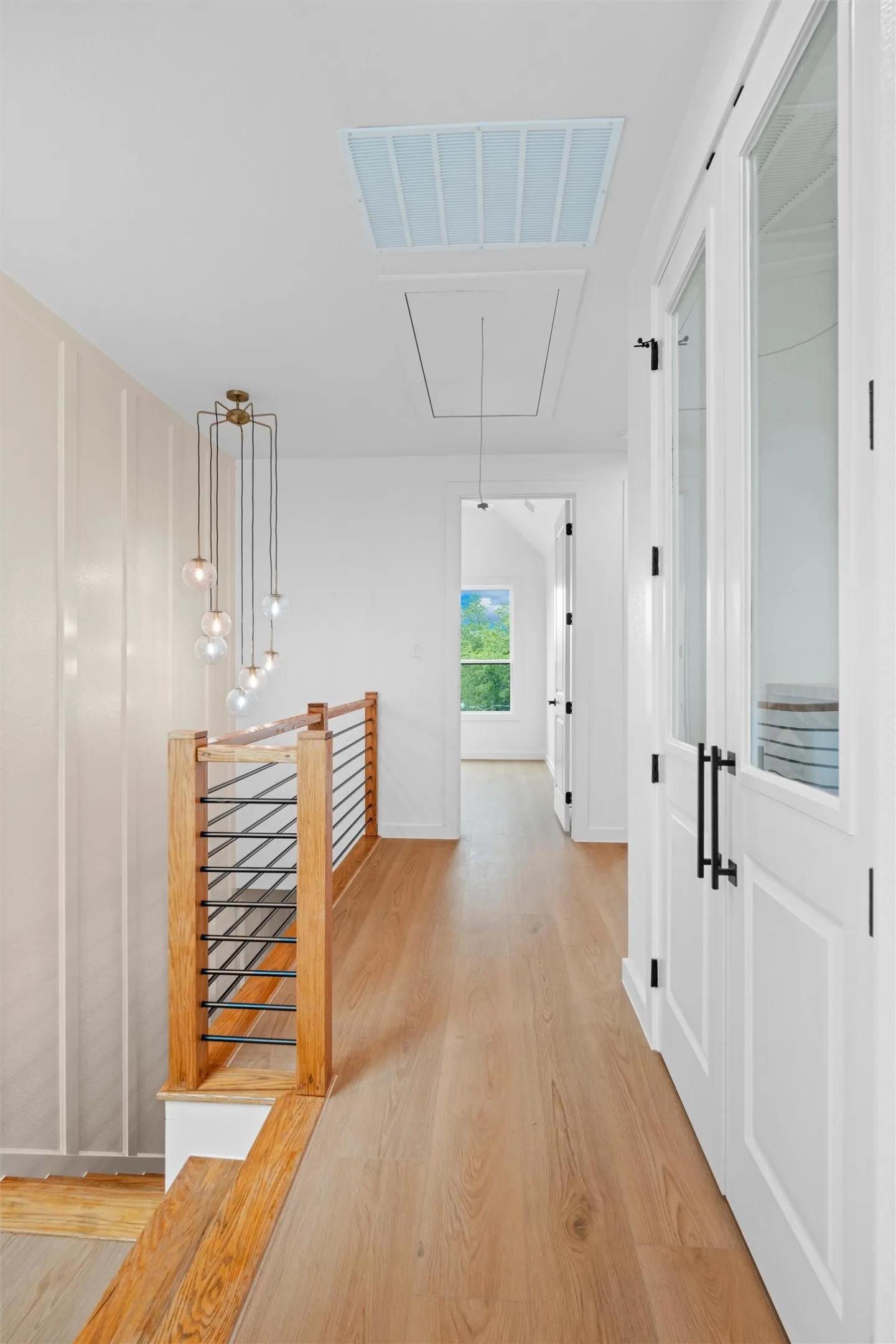 Hardwood flooring extends throughout this upper-level hallway, complemented by a modern chandelier and a wood-and-metal cable railing system