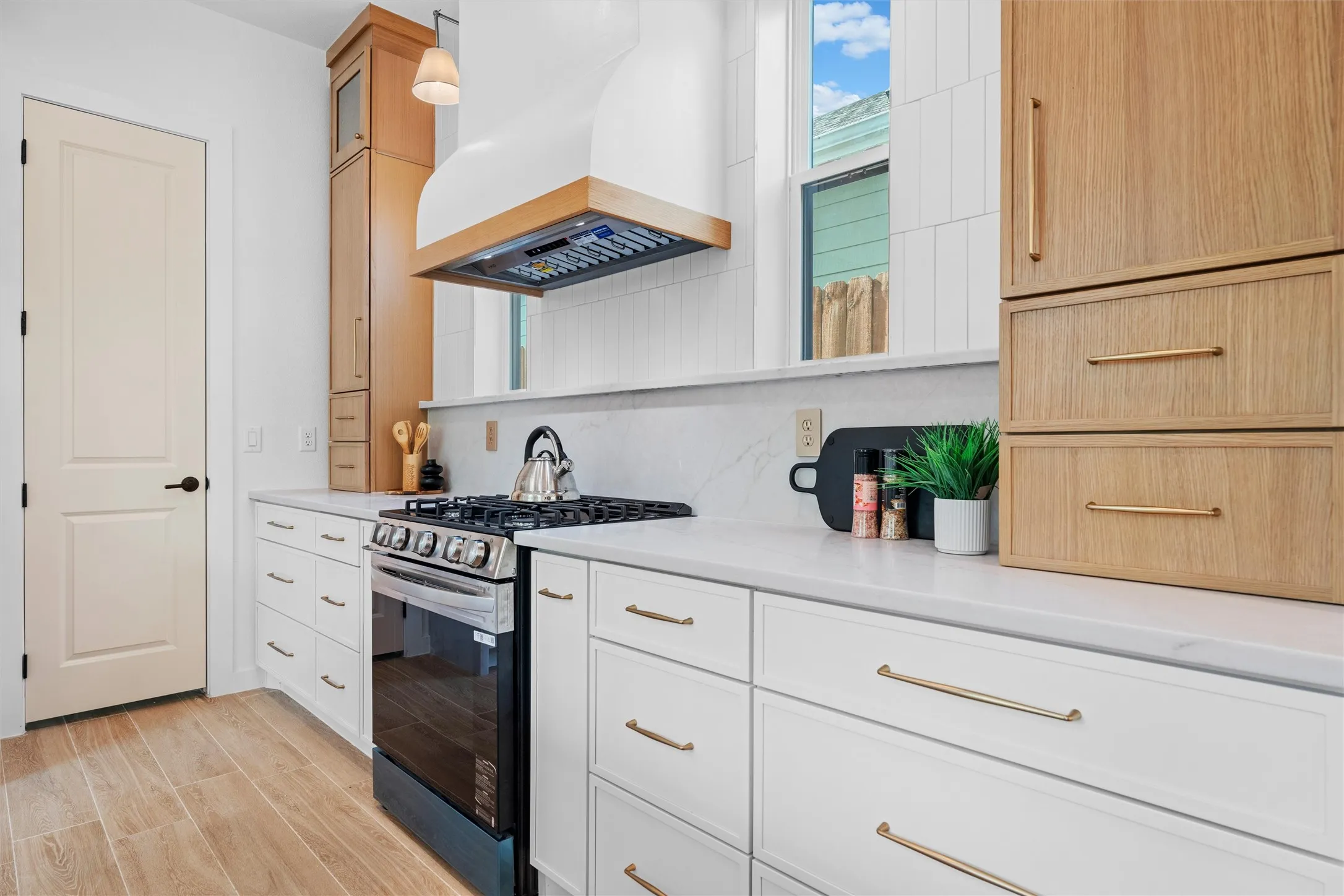 Gourmet kitchen featuring a stainless steel range, white shaker-style cabinetry with gold-tone hardware, wood-finish flooring, white countertop, and a custom range hood