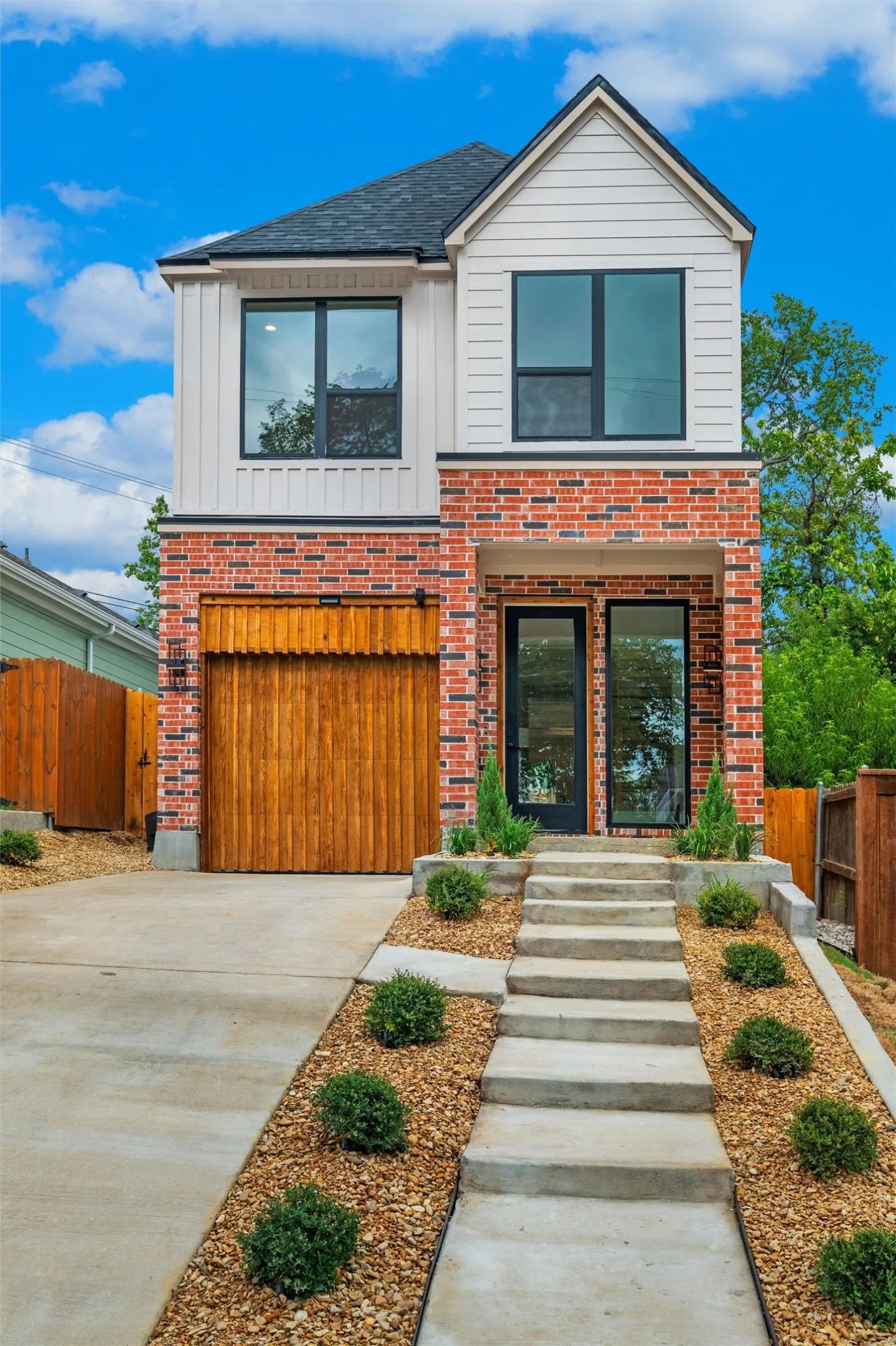 Contemporary two-story residence featuring a brick and vertical siding facade, black-framed windows, and a black front door with glass panels