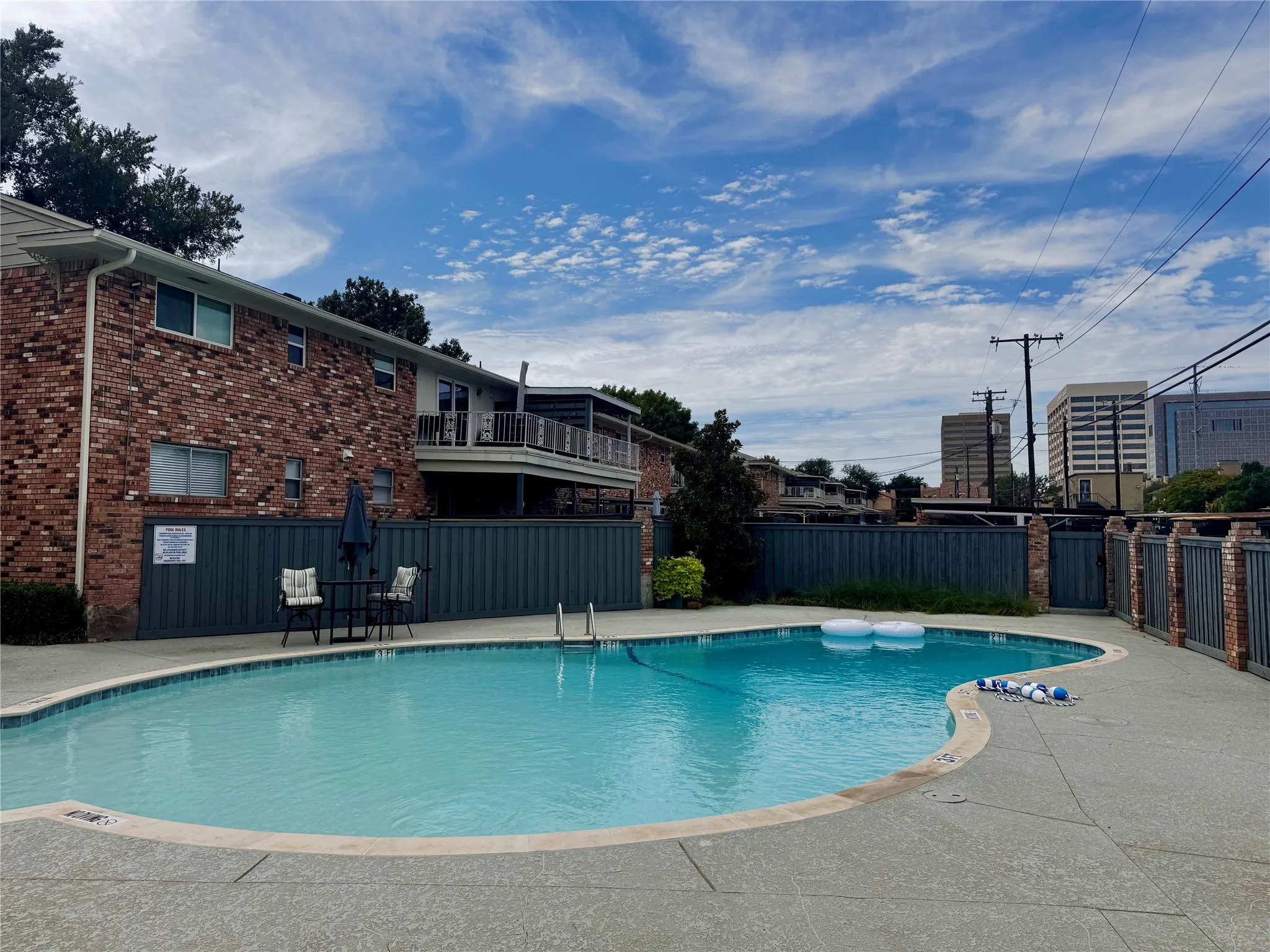 Curved swimming pool with concrete decking, brick fencing, and a red brick exterior building