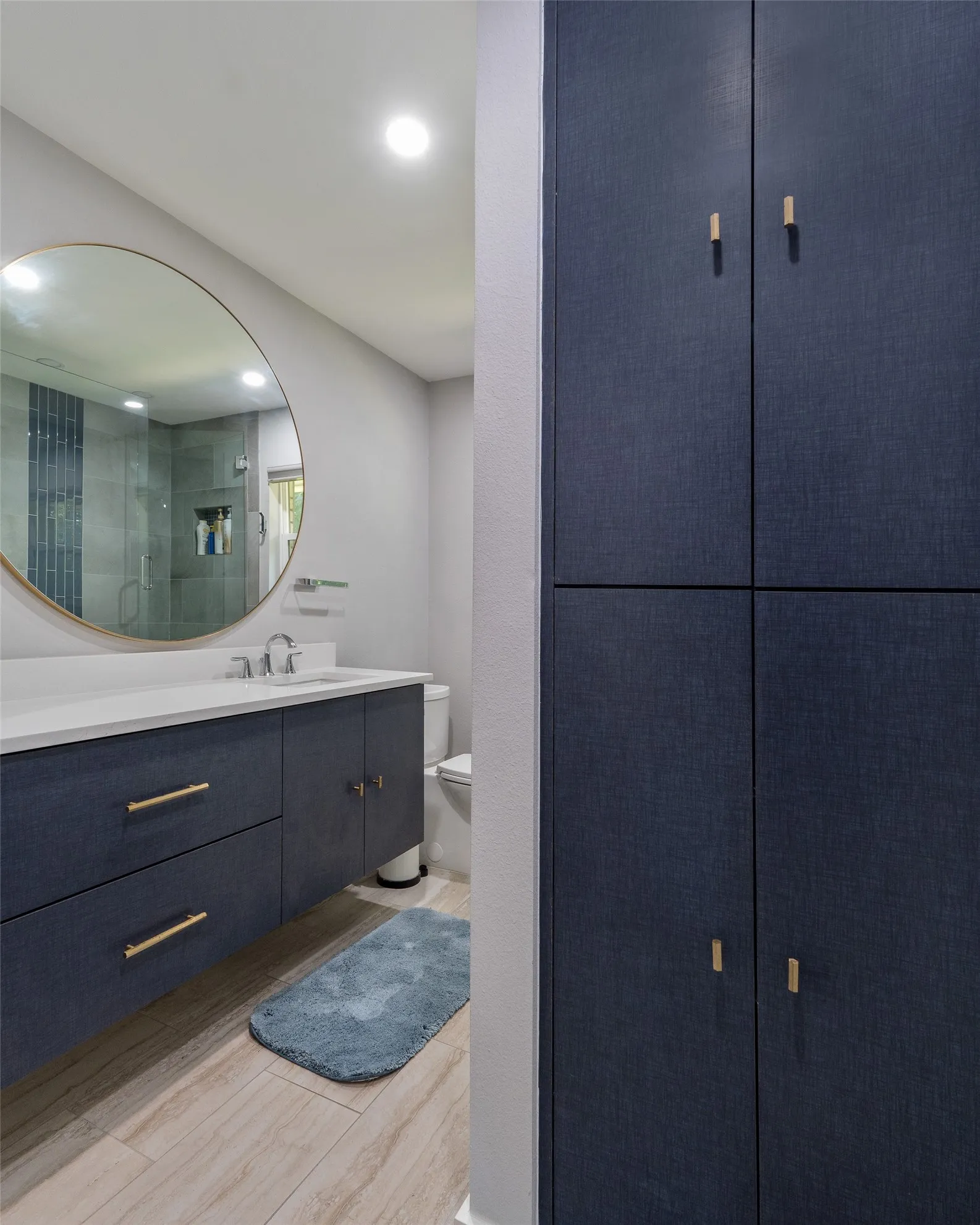 Built-in floor-to-ceiling cabinetry, floating vanity with gold-tone hardware, vessel sink, and an expansive round mirror
