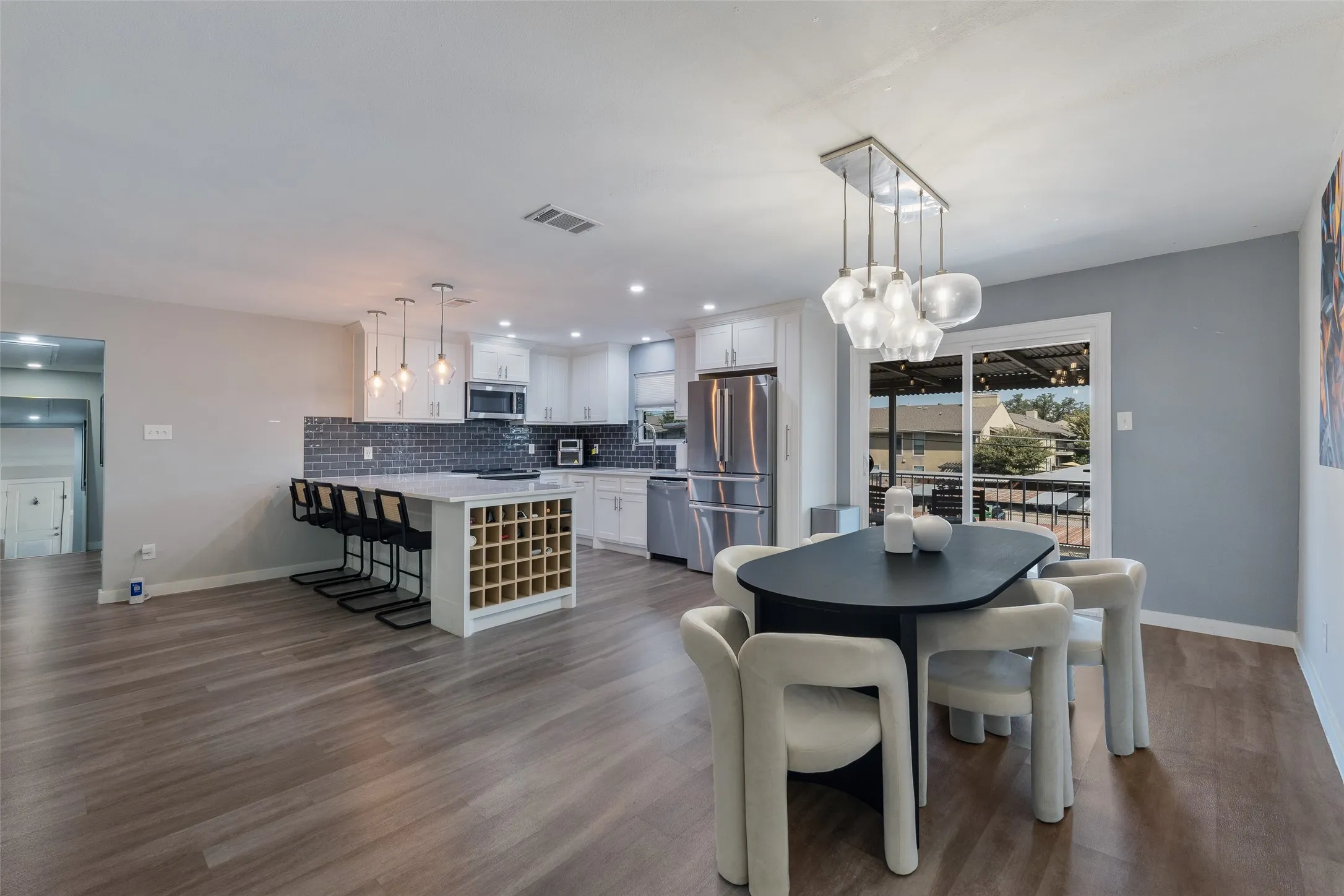 Open-concept kitchen and dining area featuring wood-finish flooring, white cabinetry, a kitchen island with built-in wine storage, and a sliding glass door