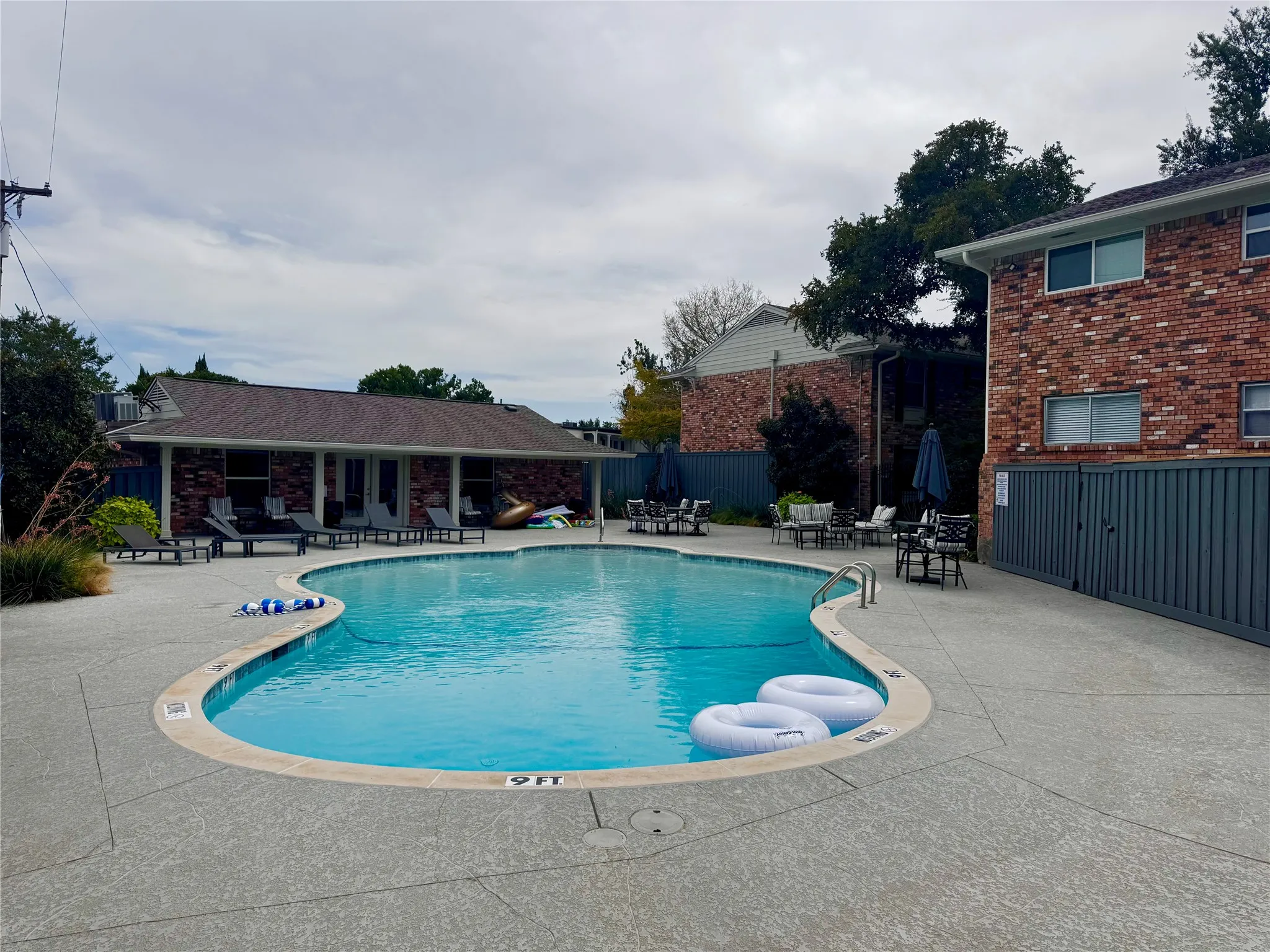Resort-style pool with a curved edge, surrounding concrete decking, and adjacent brick buildings