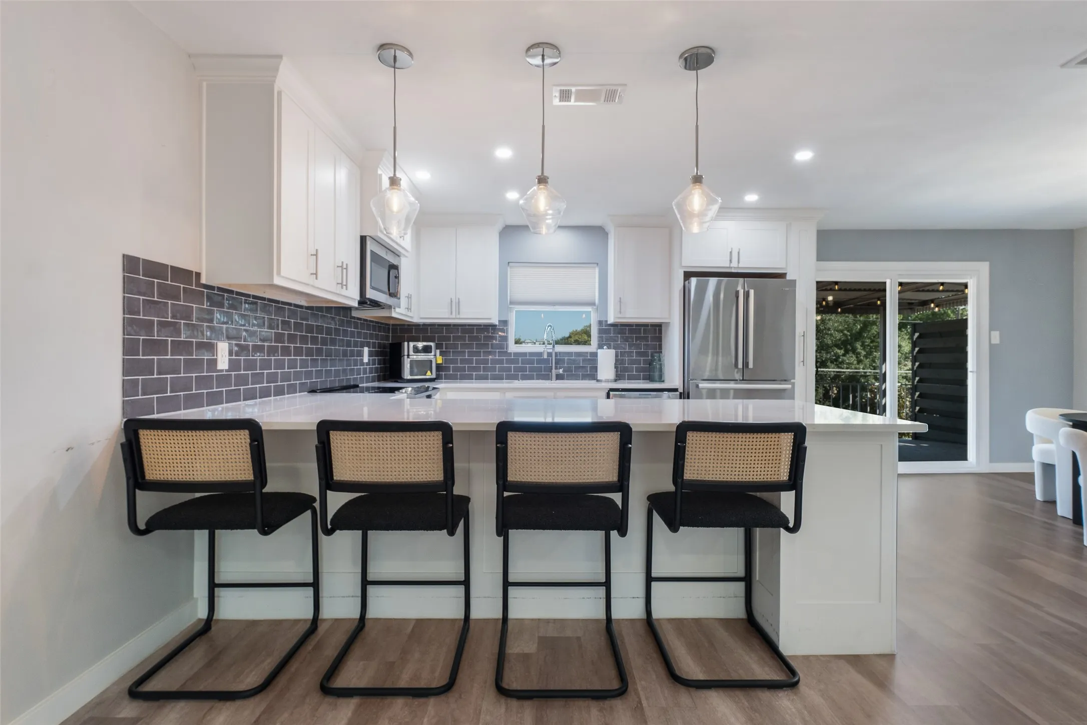 White shaker cabinetry, dark subway tile backsplash, stainless steel appliances, pendant lighting, and wood-finish flooring