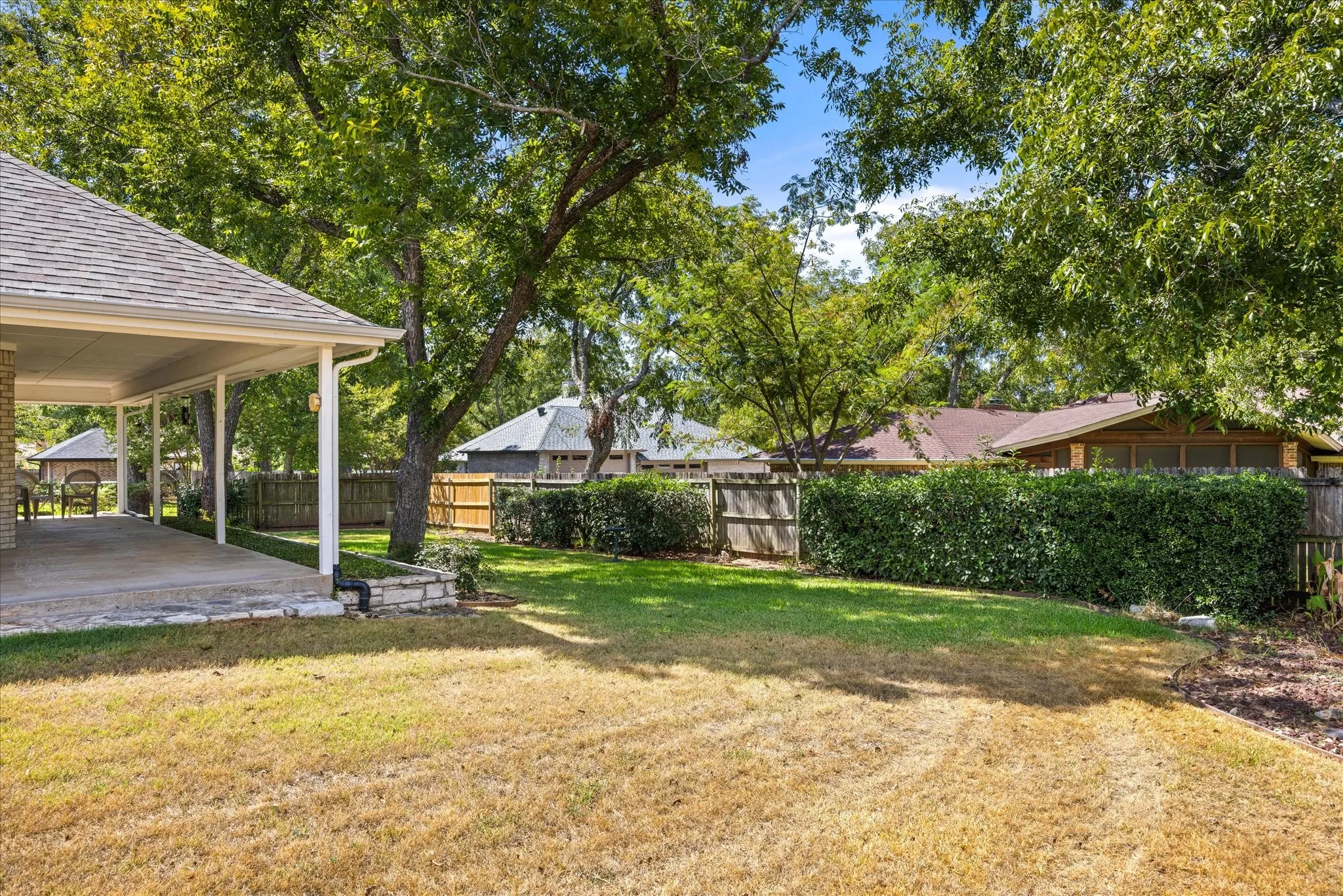 Expansive backyard featuring mature trees, a covered patio, and privacy fencing with established hedges