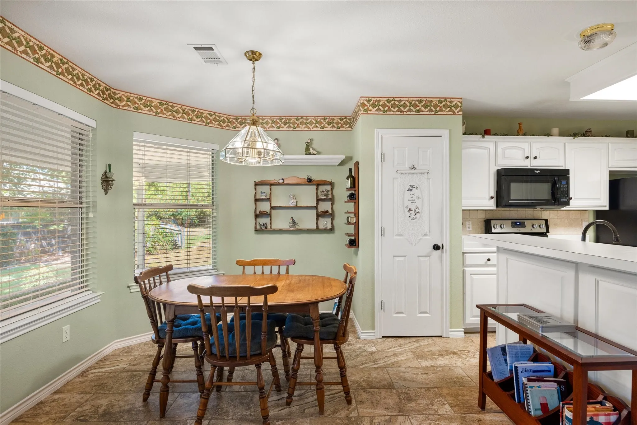 Kitchen dining area featuring tile flooring, multiple windows with blinds, a hanging pendant light fixture, white cabinetry, and built-in appliances