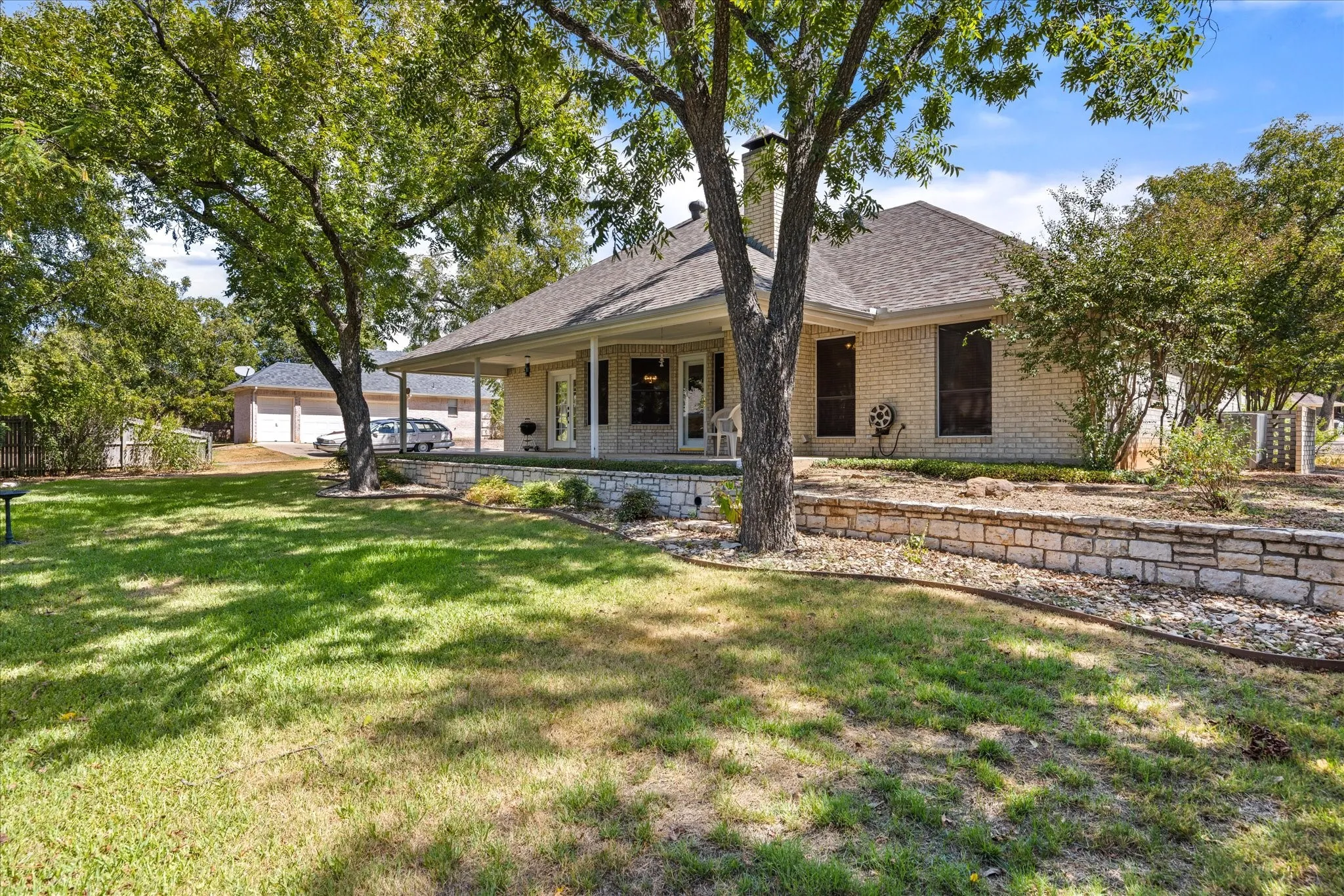 Brick exterior, covered front porch, stone retaining wall, mature trees, detached garage