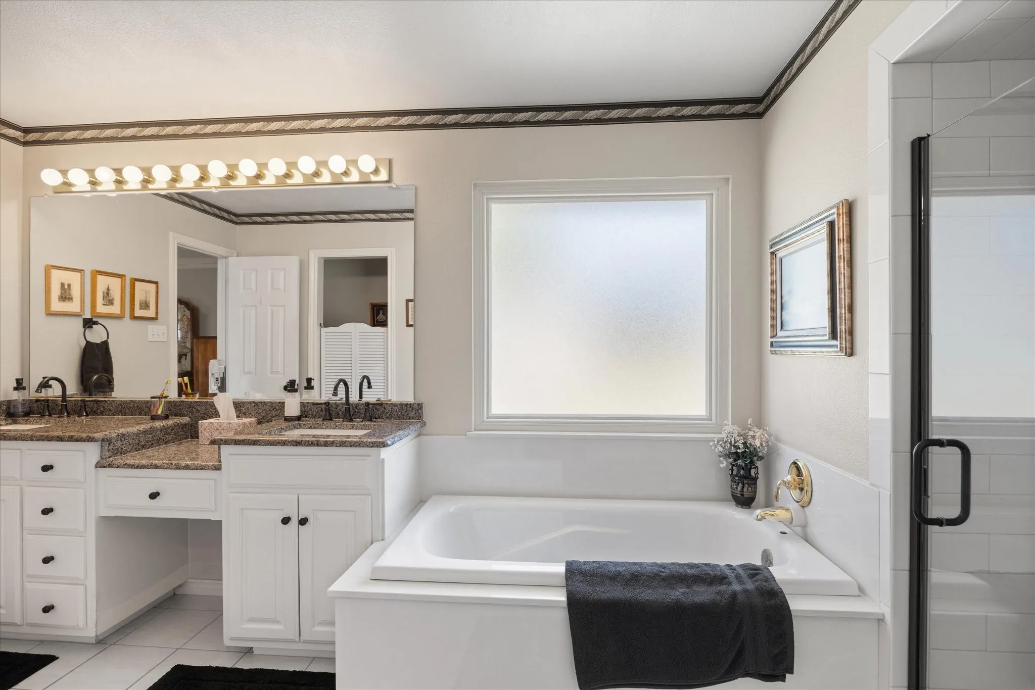 Dual vanity with granite countertops and undermount sinks, white cabinetry, and a built-in soaking tub with gold-tone fixtures